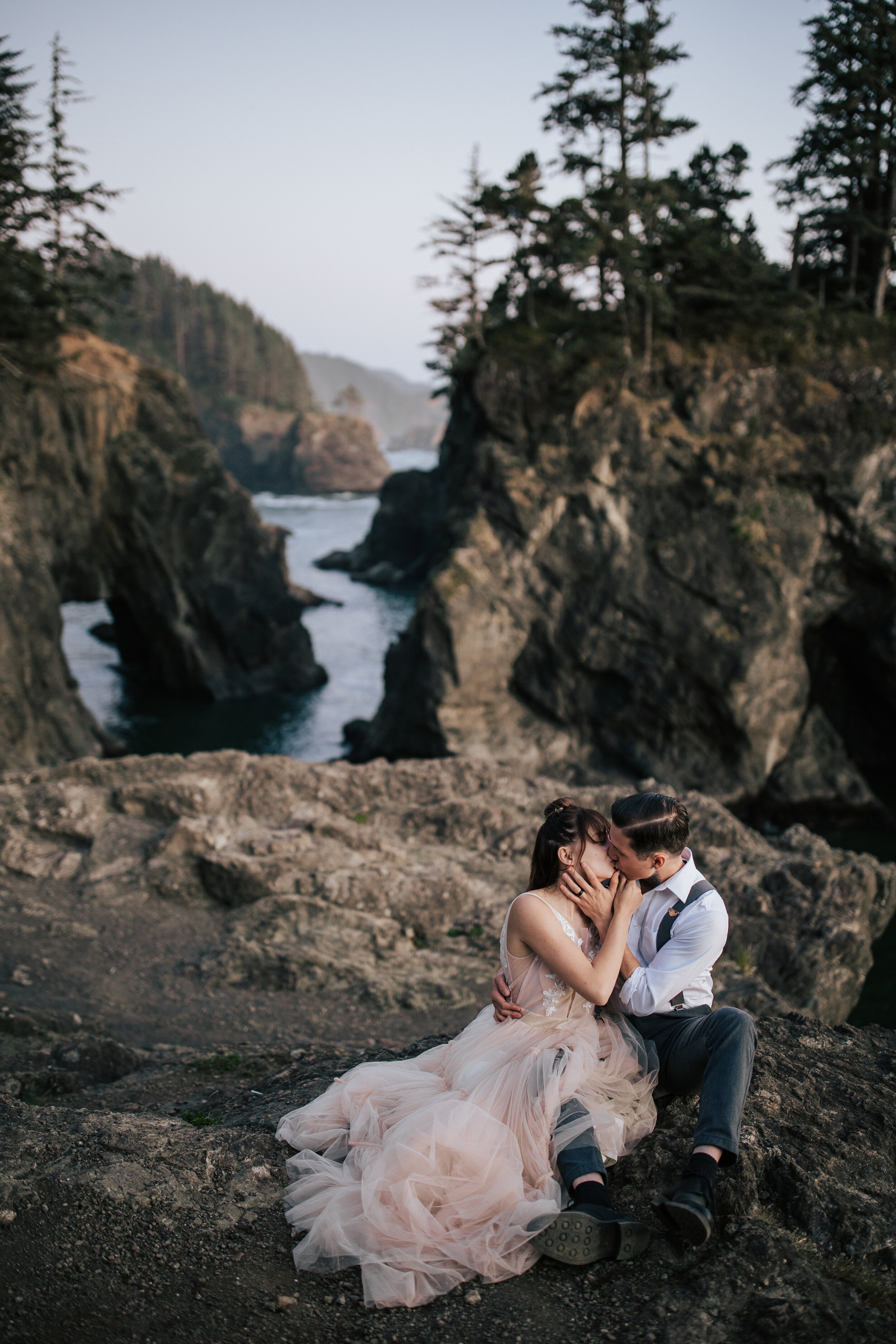  In Oregon Emily Jenkins Photography captures a woman in a blush gown and man in suspenders kissing during an elopement. blush wedding gowns suspenders for groom Oregon coast elopements elopement style #emilyjenkinsphotography #emilyjenkinselopements