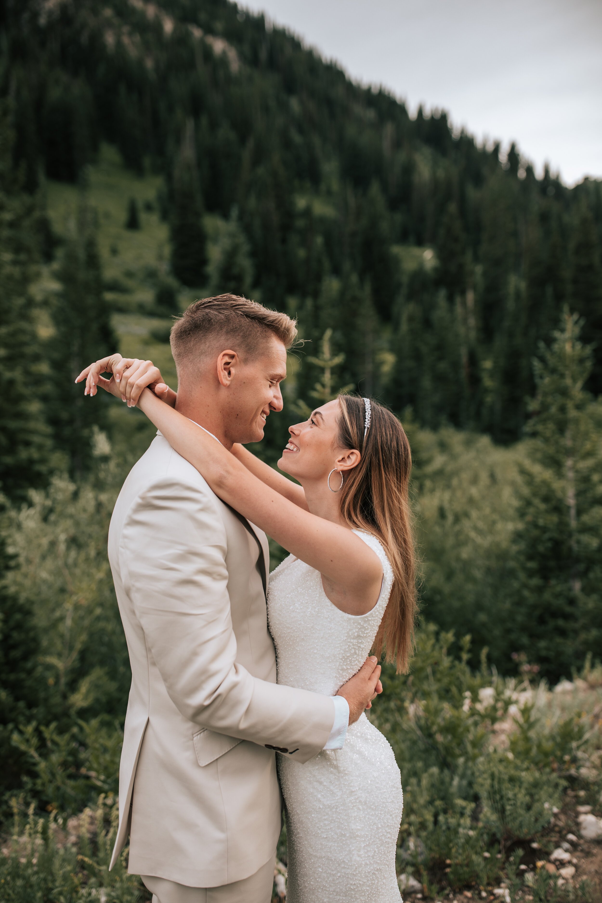  In the mountains or Northern Utah a bride puts her arms around her groom and looks lovingly into his eyes by Emily Jenkins Photography. elope in the mountains elopement locations fitted wedding gown #emilyjenkinsphotography #emilyjenkinselopements #