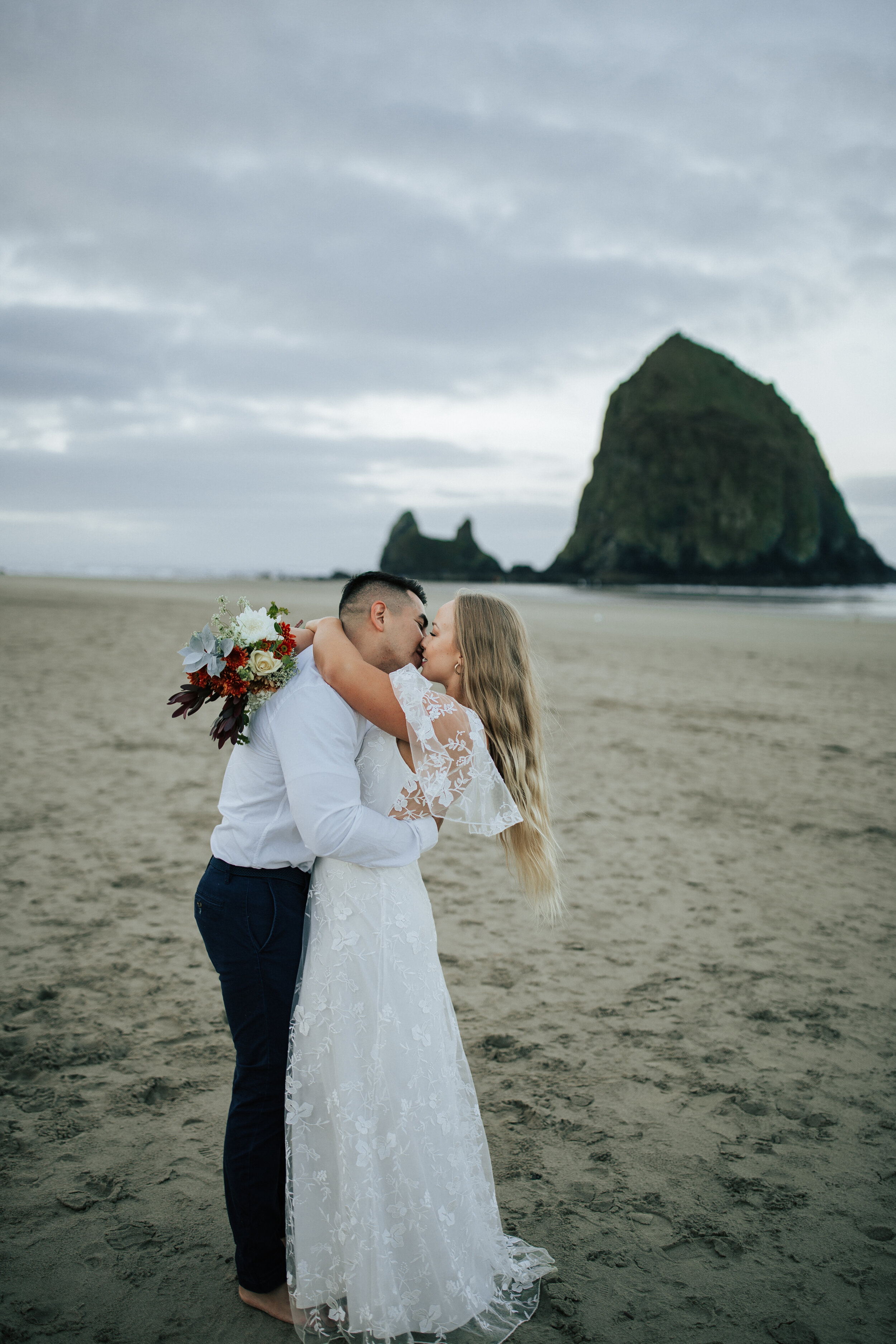  With a beautiful light and flouncy wedding dress a bride kisses her groom on an Oregon Beach during an elopement by Emily Jenkins Photography. floral wedding dress beach elopements beach wedding west coast beach elopement #emilyjenkinsphotography #e