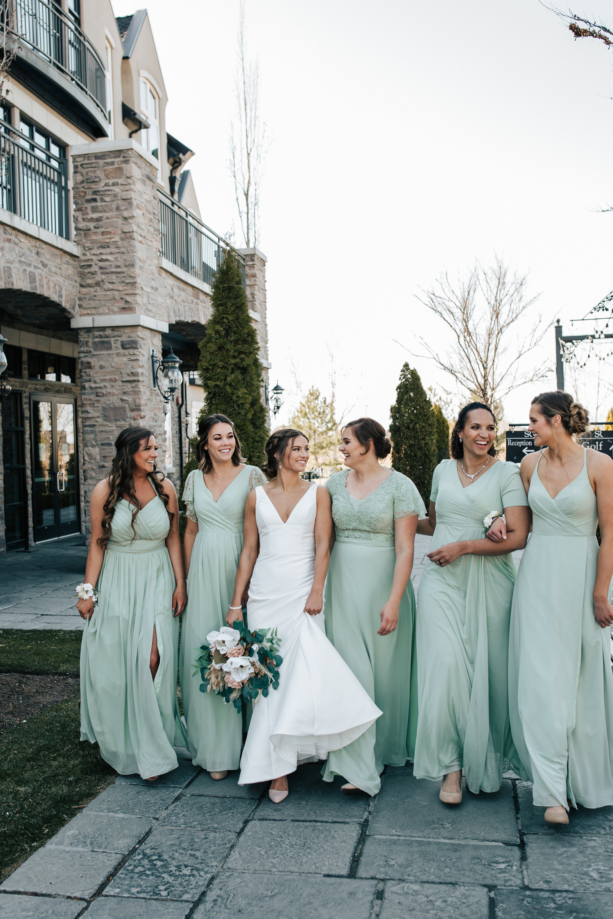  Bride in sleek and classy wedding gown walks and laughs with her bridesmaids who are wearing a light green color in Utah County at Sleepy Ridge Golf Course. bride and bridesmaids light green bridesmaids dresses #emilyjenkinsphotography #emilyjenkins