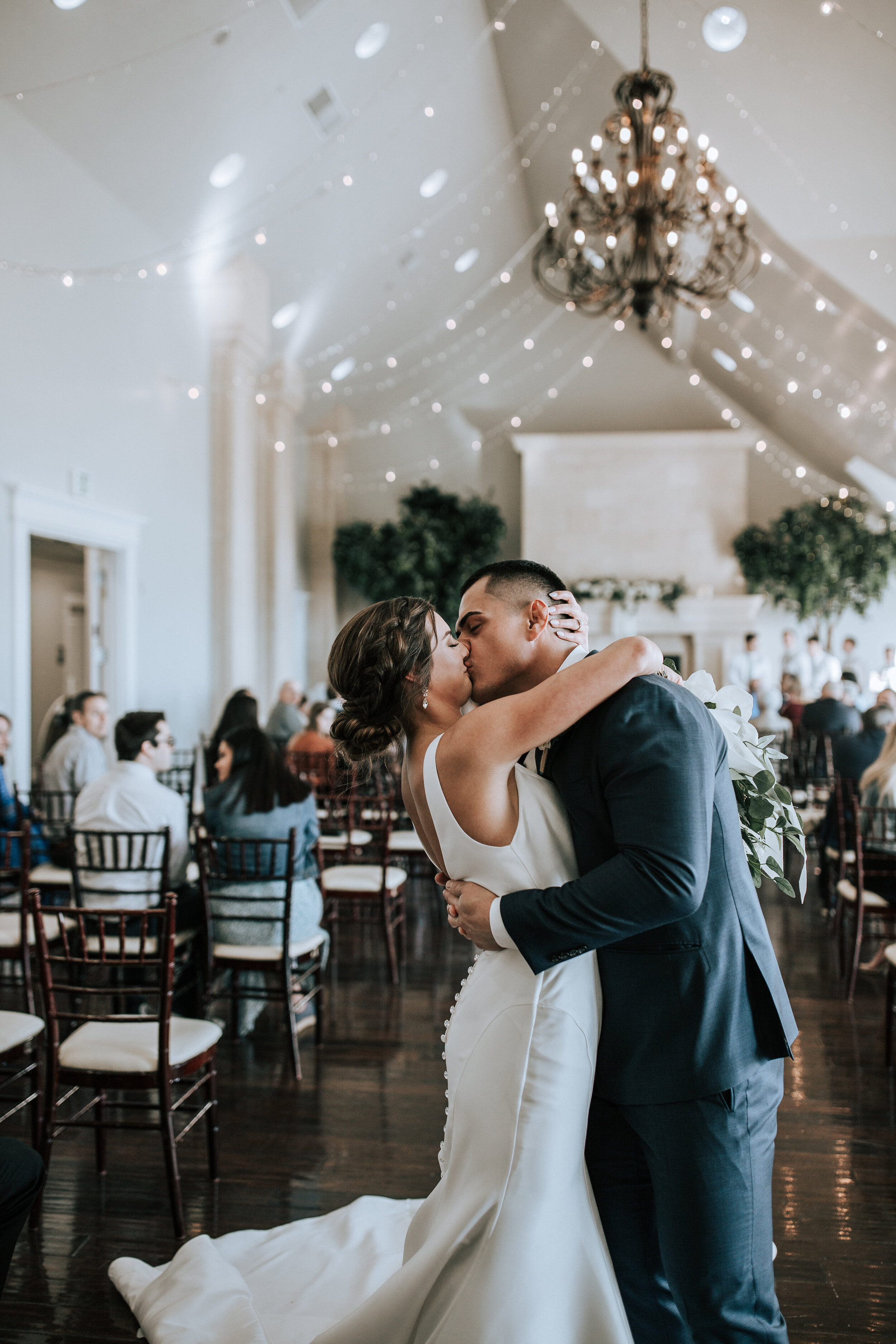  At Sleepy Ridge Golf Course a bride kisses her groom passionately under a lighted ceiling with a chandelier. buttons down the back wedding dress lights on the ceiling black suit black chairs for ceremony #emilyjenkinsphotography #emilyjenkinswedding