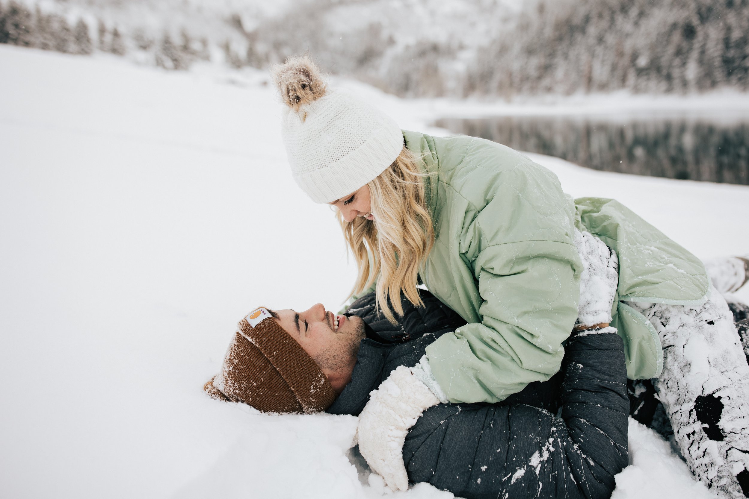  Winter engagement session at Tibble Fork Reservoir near Park City, Utah. Couple playing in the snow Snowball fight during couples photoshoot in the Utah mountains couple hugs as it's snowing covered in snowflakes engagement session winter outfit ins