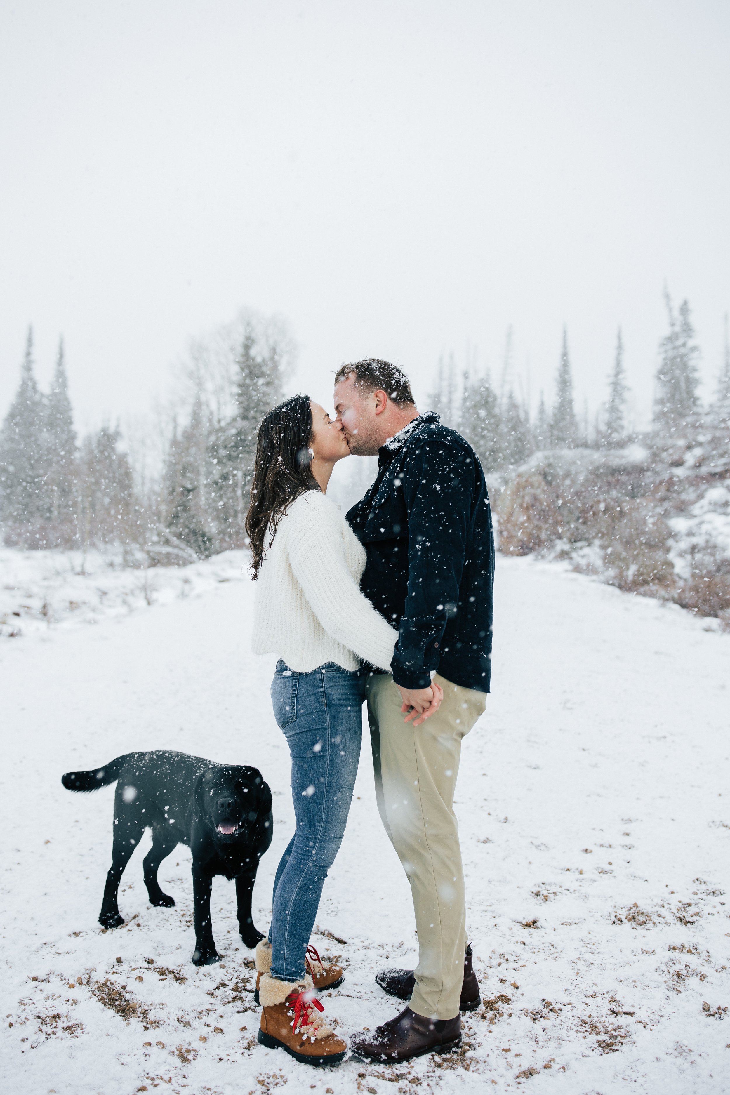  Winter photoshoot outfit inspo man holds his fiance in the mountains around pine trees and snow couples session couple playing in the snow winter engagement session #winteroutfitinspo #outfitinspo #winteroutfits #winterphotoshoot a couple kisses wit