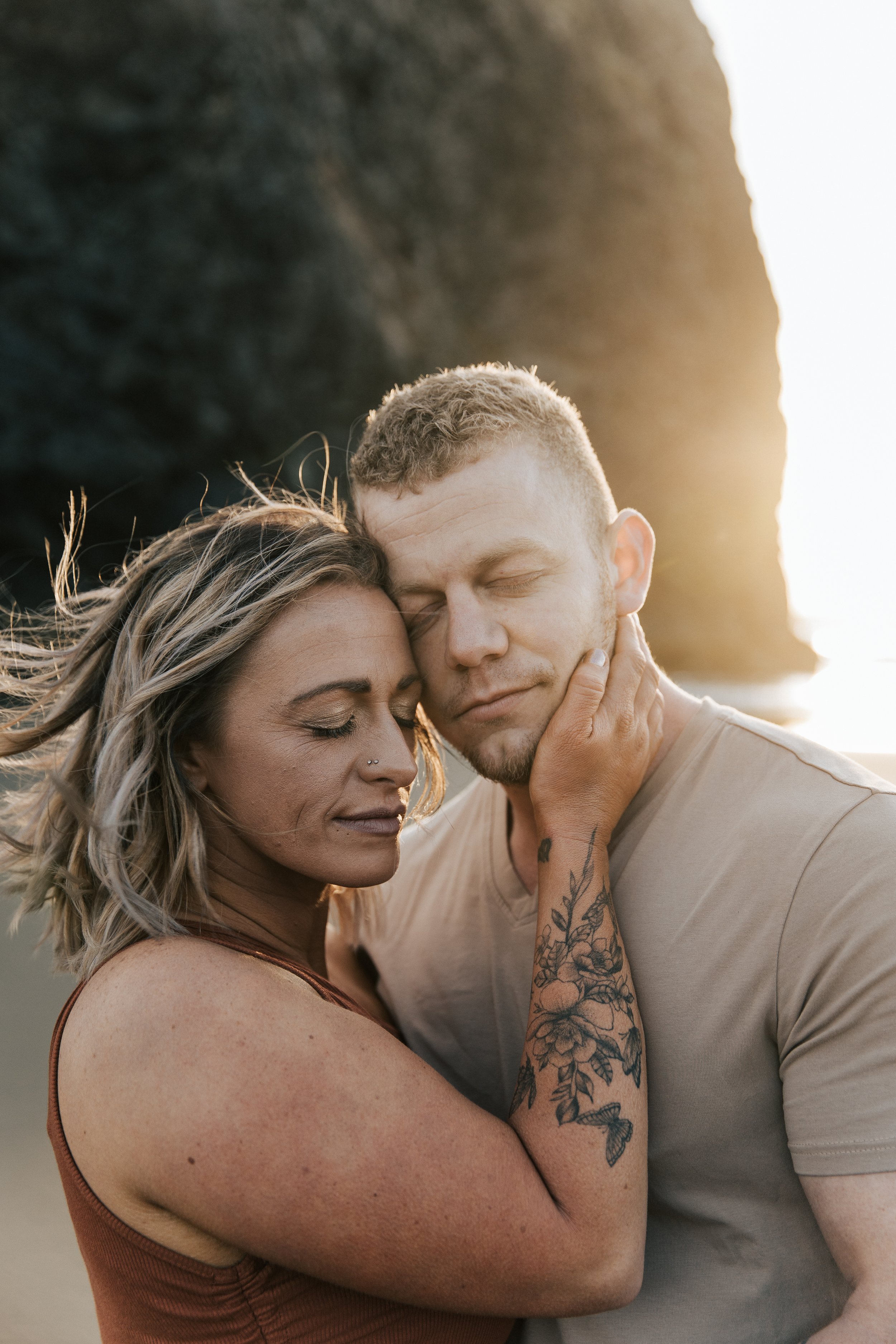  Brookings, Oregon engagement session. Couple hugs on the beach for a summer couples session on their anniversary. Husband and wife run around the beach with seastacks and rocks on the beach around them, barefoot in the sand.  