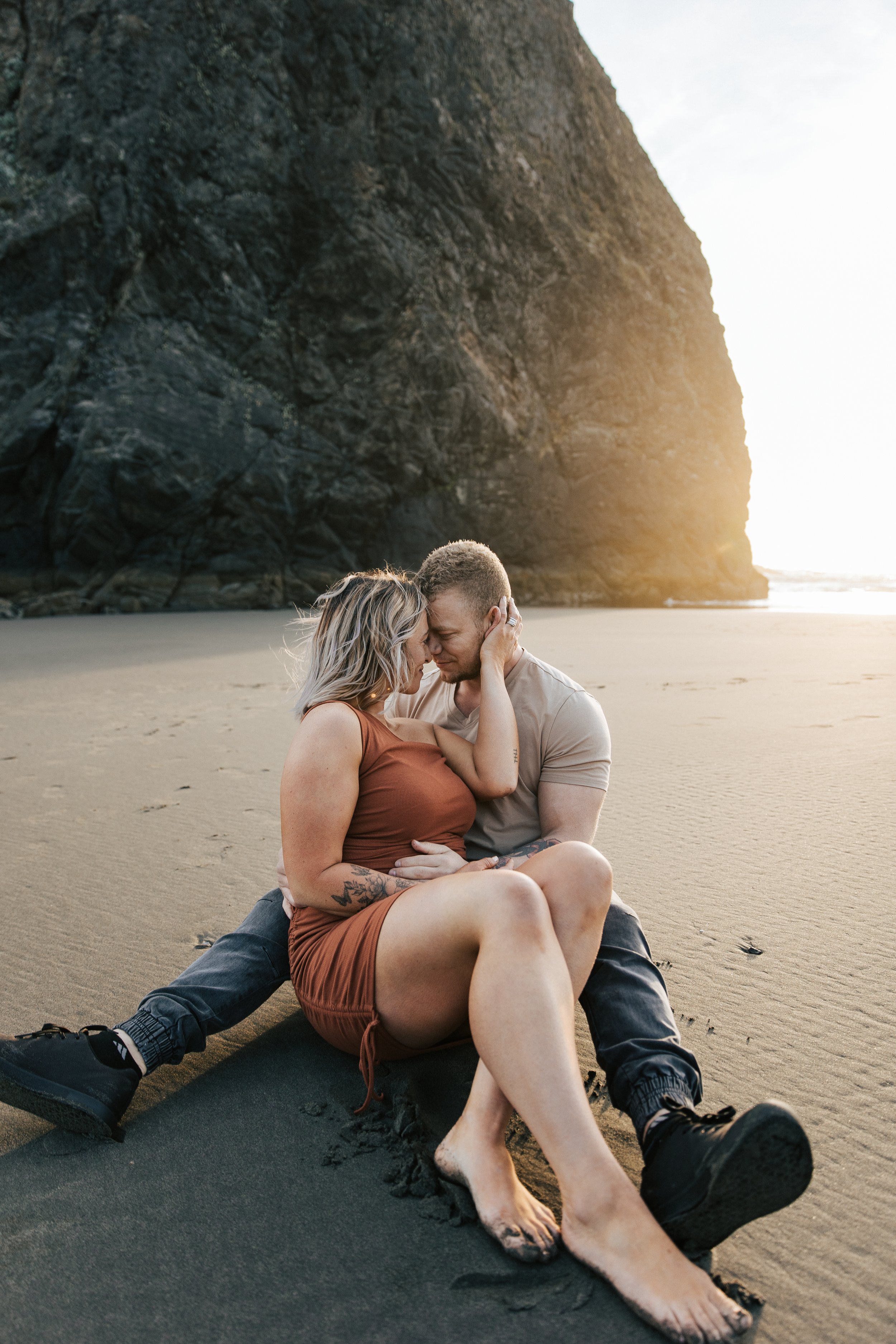  Brookings, Oregon engagement session. Couple cuddles on the beach for a summer couples session on their anniversary. Husband and wife run around the beach with seastacks and rocks on the beach around them, barefoot in the sand.  