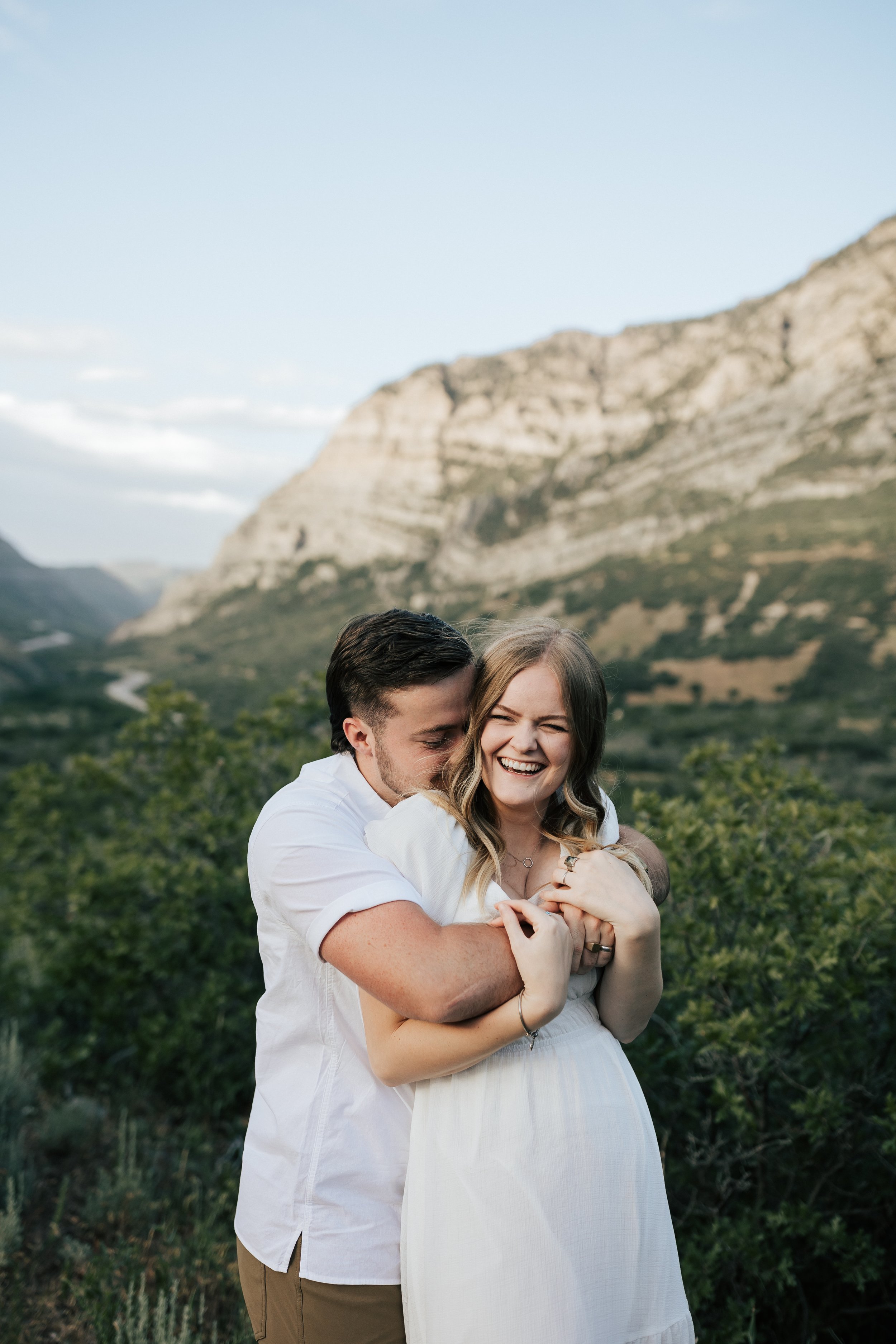  Summer anniversary couples session in the mountains. A young couple laughs together in the mountains. Utah photographer. Engagement session outfit inspo. #utahphotographer #utahengagements #outfitinspo 