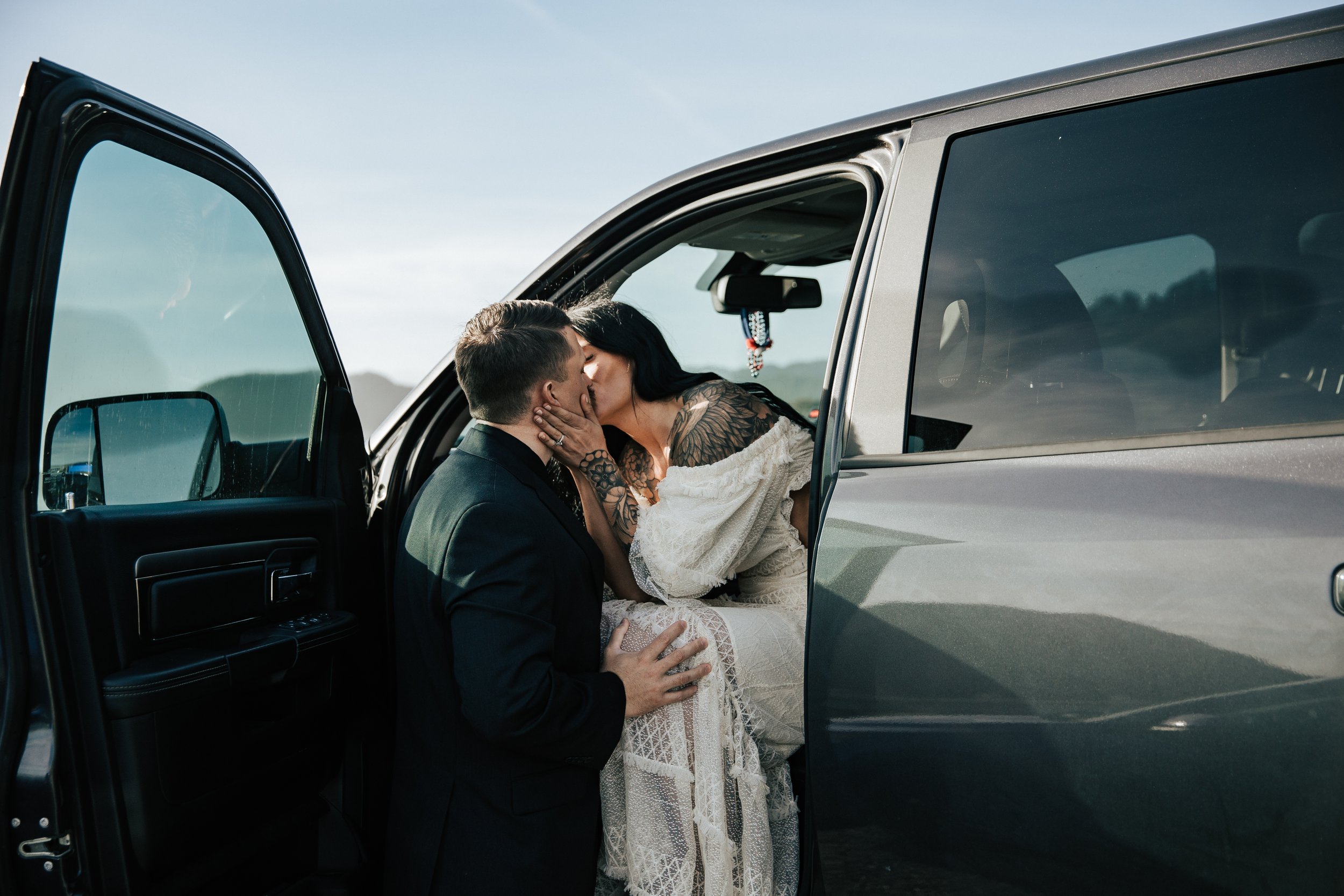  Oregon coast elopement. Couple elopes on the beach with the sun shining behind them. Sun rays behind rocks. Beach with rocks and haystacks. Southern Oregon. Couple getting to ceremony spot, kisses in truck before ceremony. 