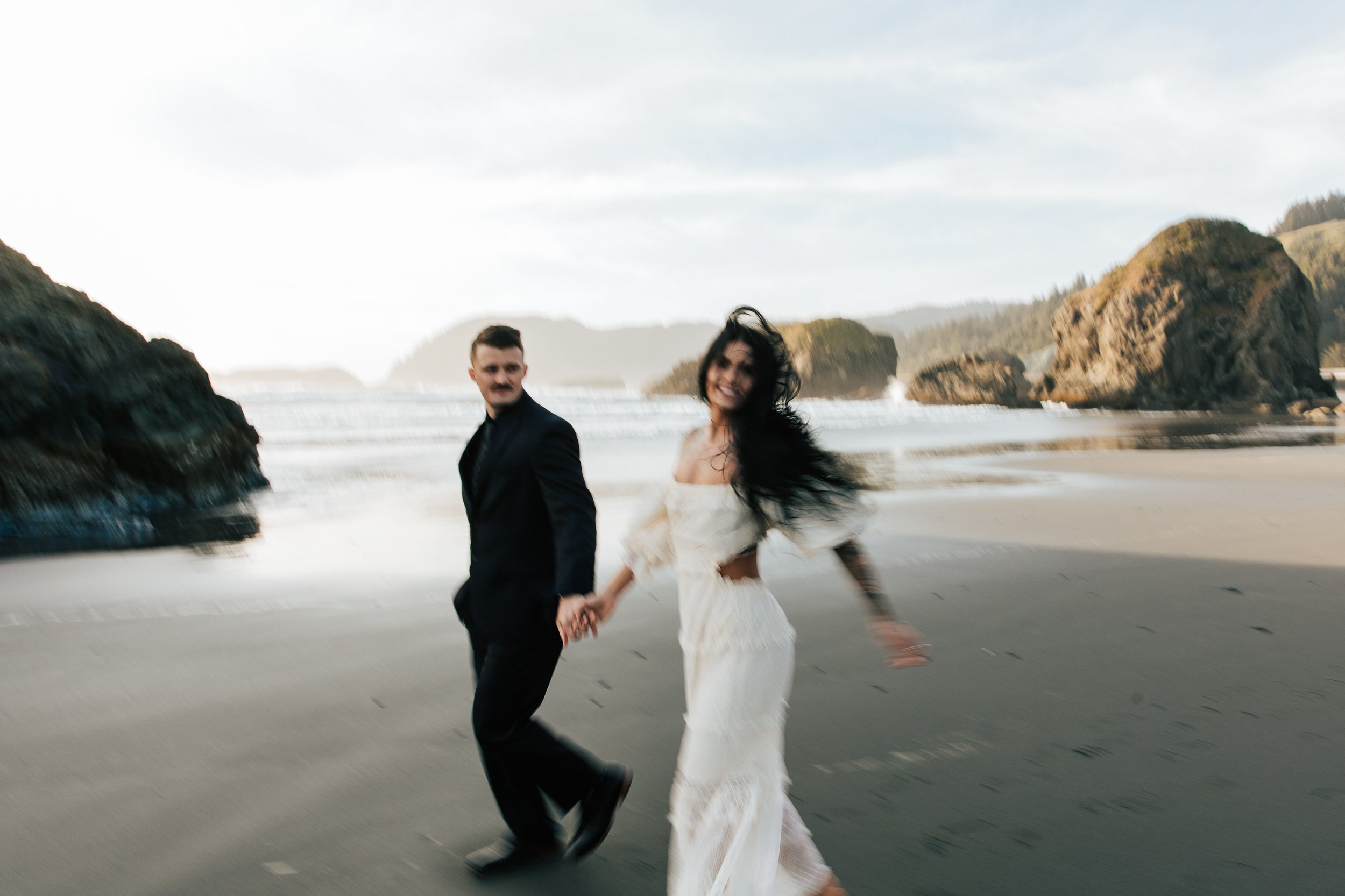  Oregon coast elopement. Couple elopes on the beach with the sun shining behind them. Sun rays behind rocks. Beach with rocks and haystacks. Southern Oregon. Golden hour photos after elopement ceremony. Couple laughs together on the beach. #oregoncoa