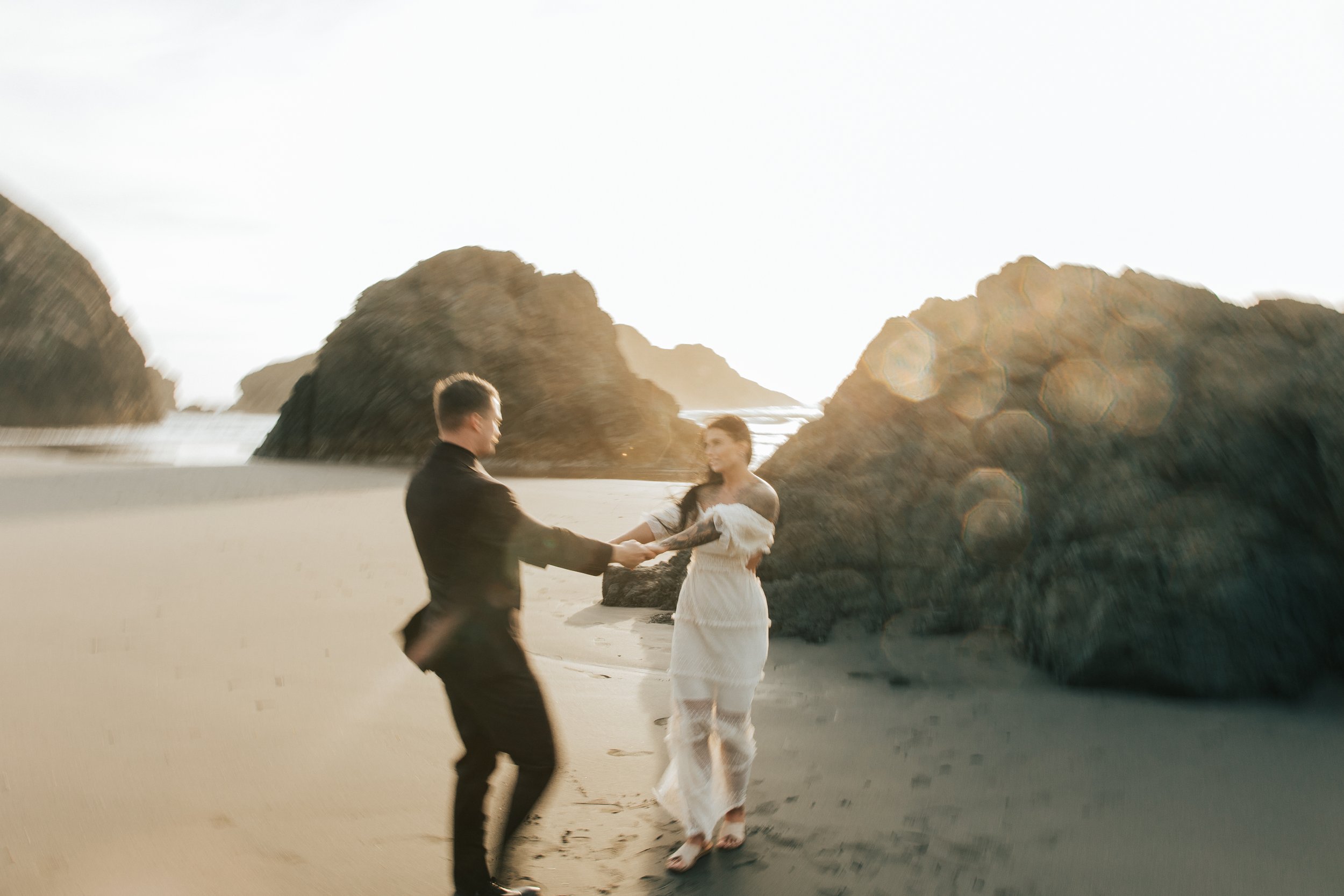  Oregon coast elopement. Couple elopes on the beach with the sun shining behind them. Sun rays behind rocks. Beach with rocks and haystacks. Southern Oregon. Couple spinning around in circles on the coast. Brookings, Oregon. Samuel H Boardman elopeme