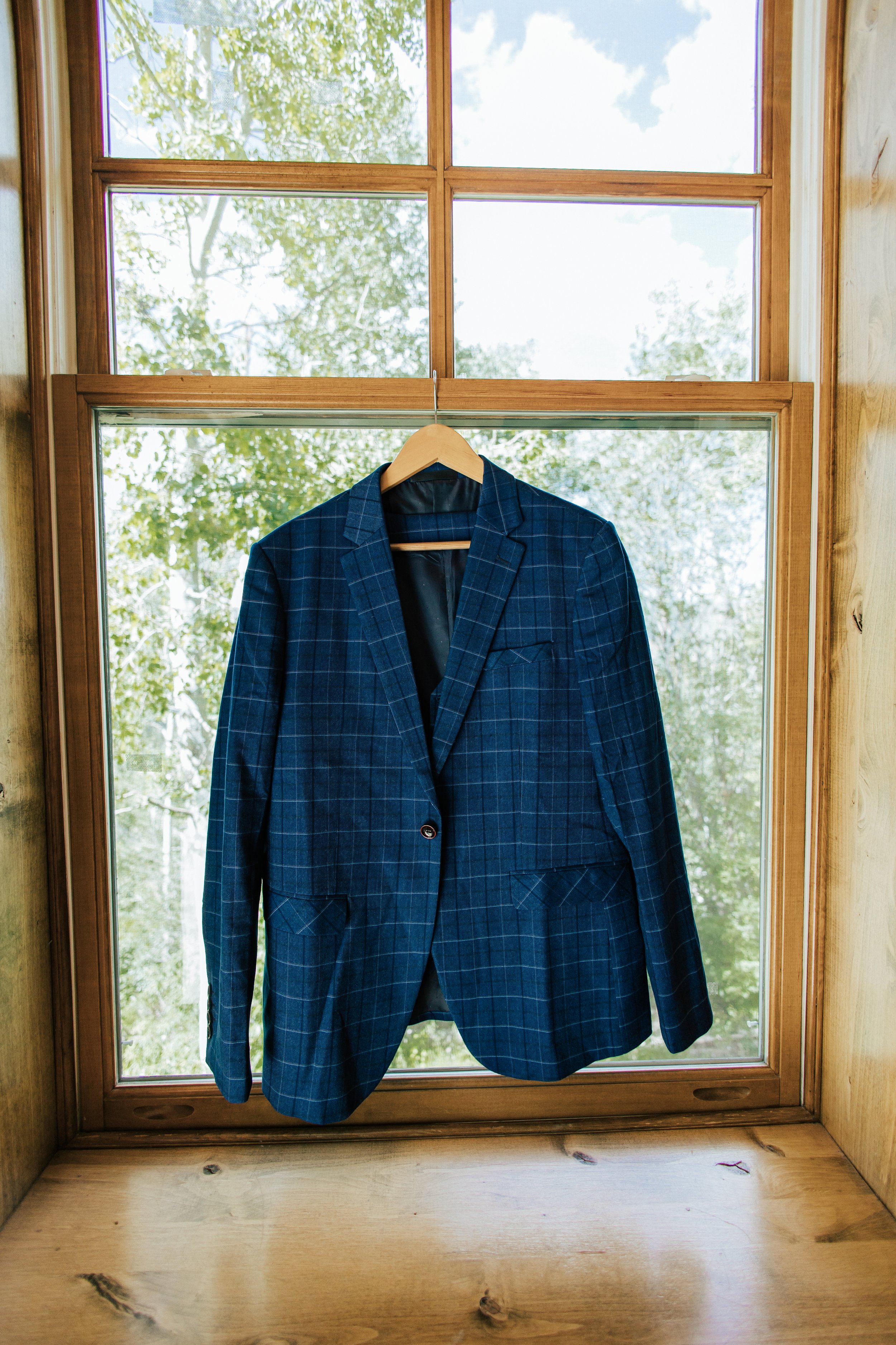  Groom’s navy blue striped suit coat hanging on window frame while groom is getting ready for wedding ceremony. 