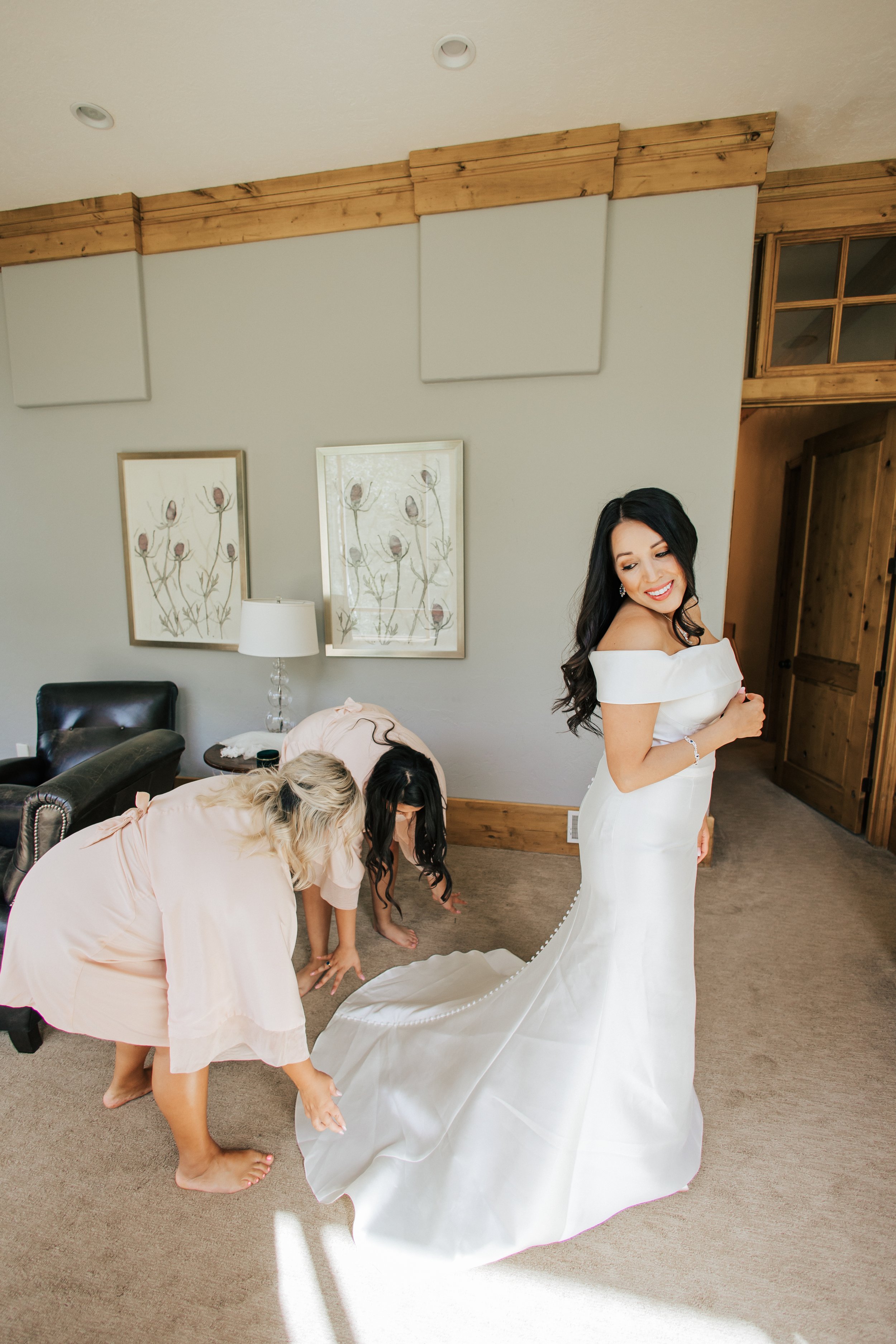  Bridemaids help bride put on her wedding dress while getting ready for her wedding ceremony in Sundance, Utah Provo Canyon. Summer wedding. 