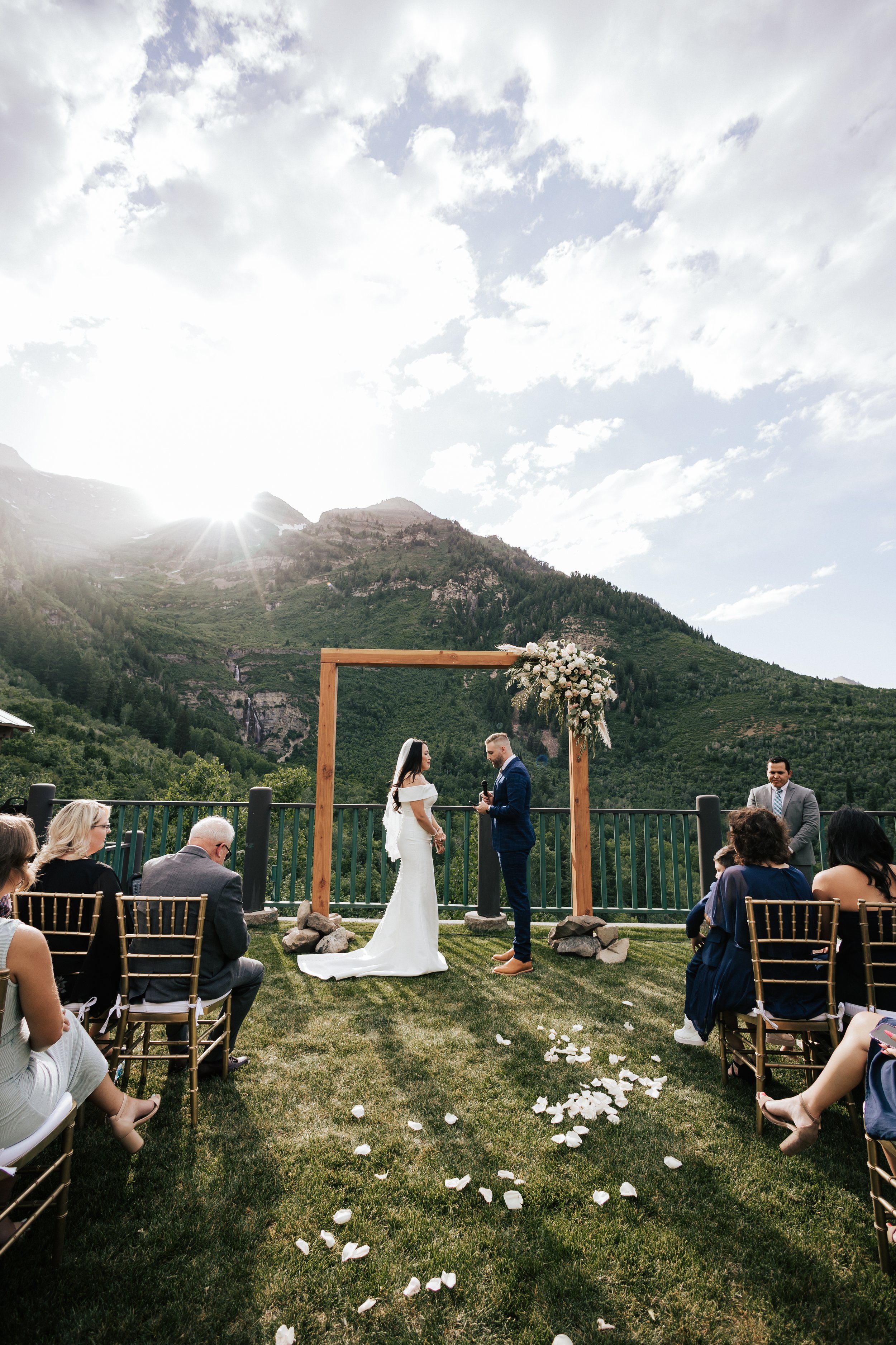  Couple exchanging vows during small, intimate wedding ceremony. Sundance, Utah wedding ceremony with the sun setting behind Mt. Timpanogos and Stewart Falls in view. Beautiful summer wedding in Provo, Utah with green mountains behind. #utahwedding #