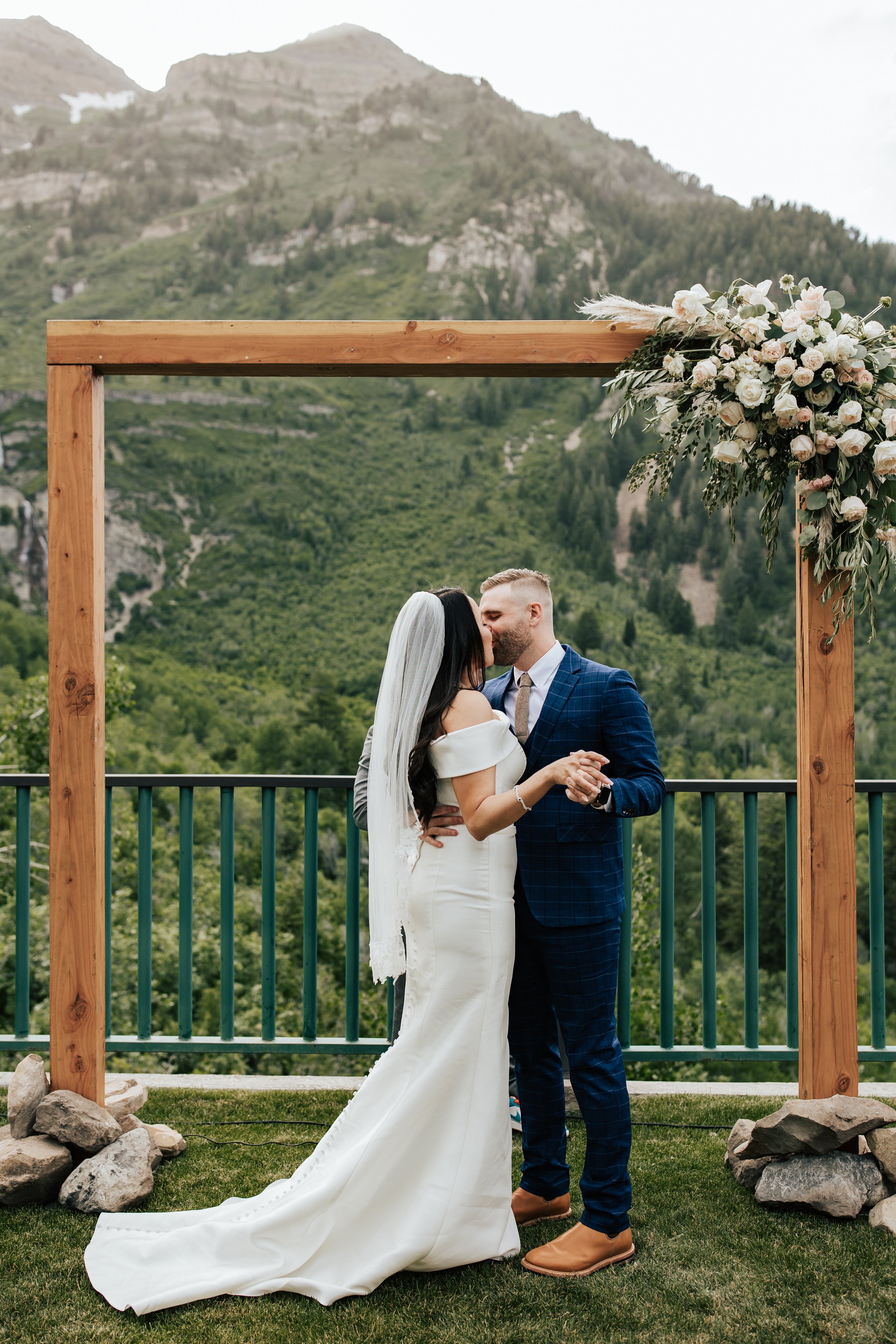  Couple’s first kiss and husband and wife at end of wedding ceremony. Sundance, Utah wedding ceremony with the sun setting behind Mt. Timpanogos and Stewart Falls in view. Beautiful summer wedding in Provo, Utah with green mountains behind. #utahwedd