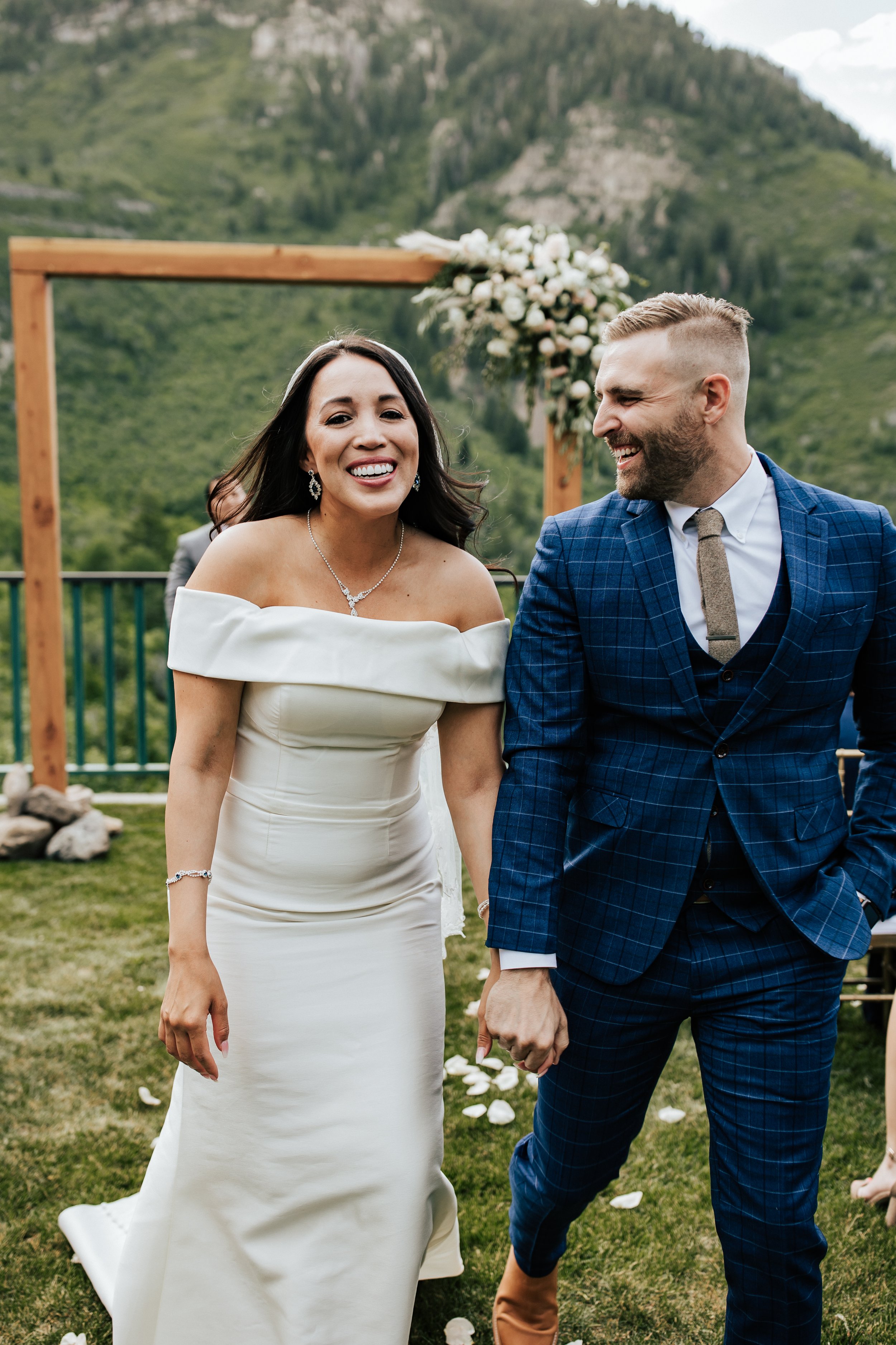  Couple walks down aisle as husband and wife after wedding ceremony. Bride and groom laugh together after getting married. Sundance, Utah wedding ceremony with the sun setting behind Mt. Timpanogos and Stewart Falls in view. Beautiful summer wedding 