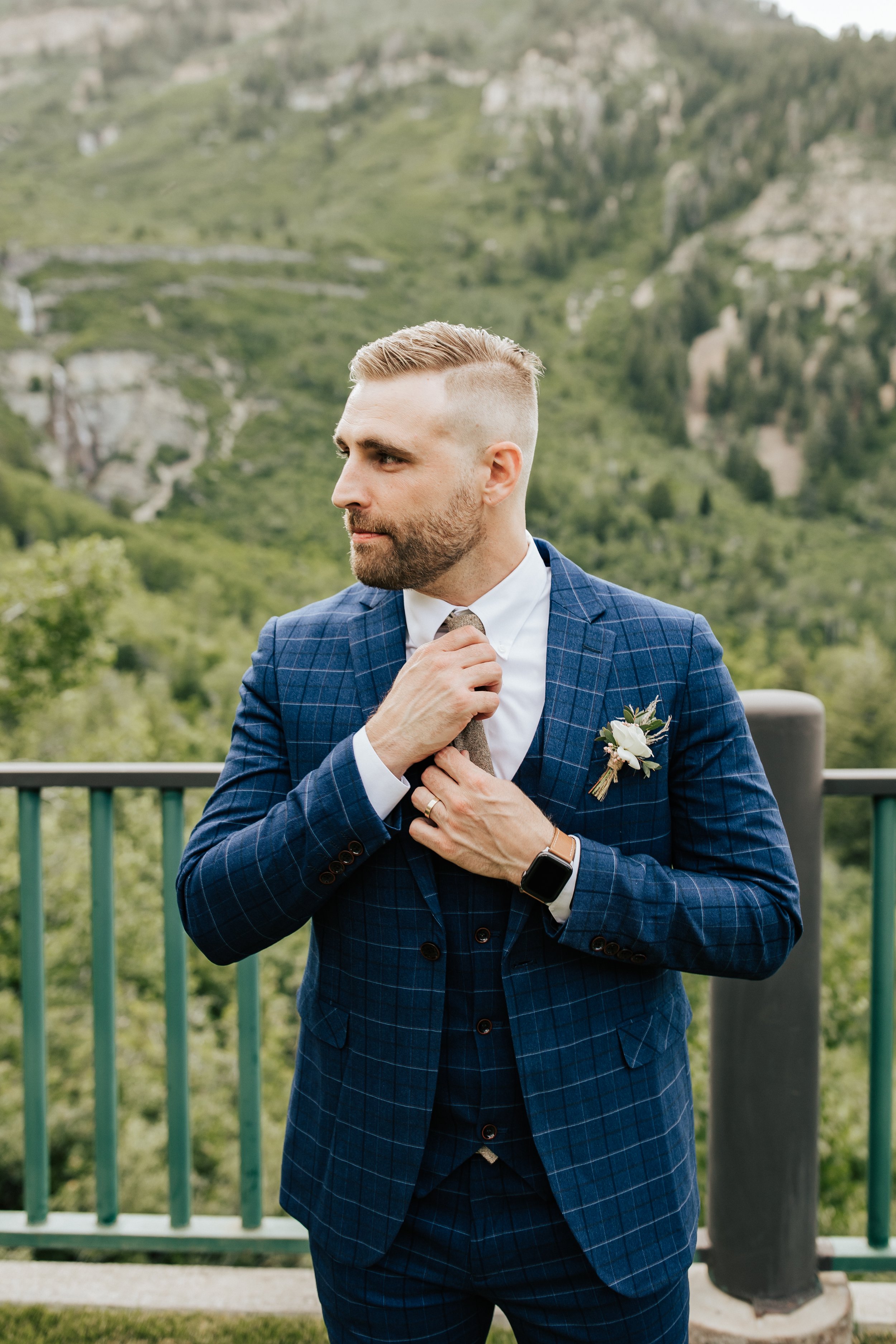  Groom adjusting tie after getting married. Groom wears a striped navy blue suit, a watch, and a corsage. #weddingphotos #weddingphotographer #utahwedding 