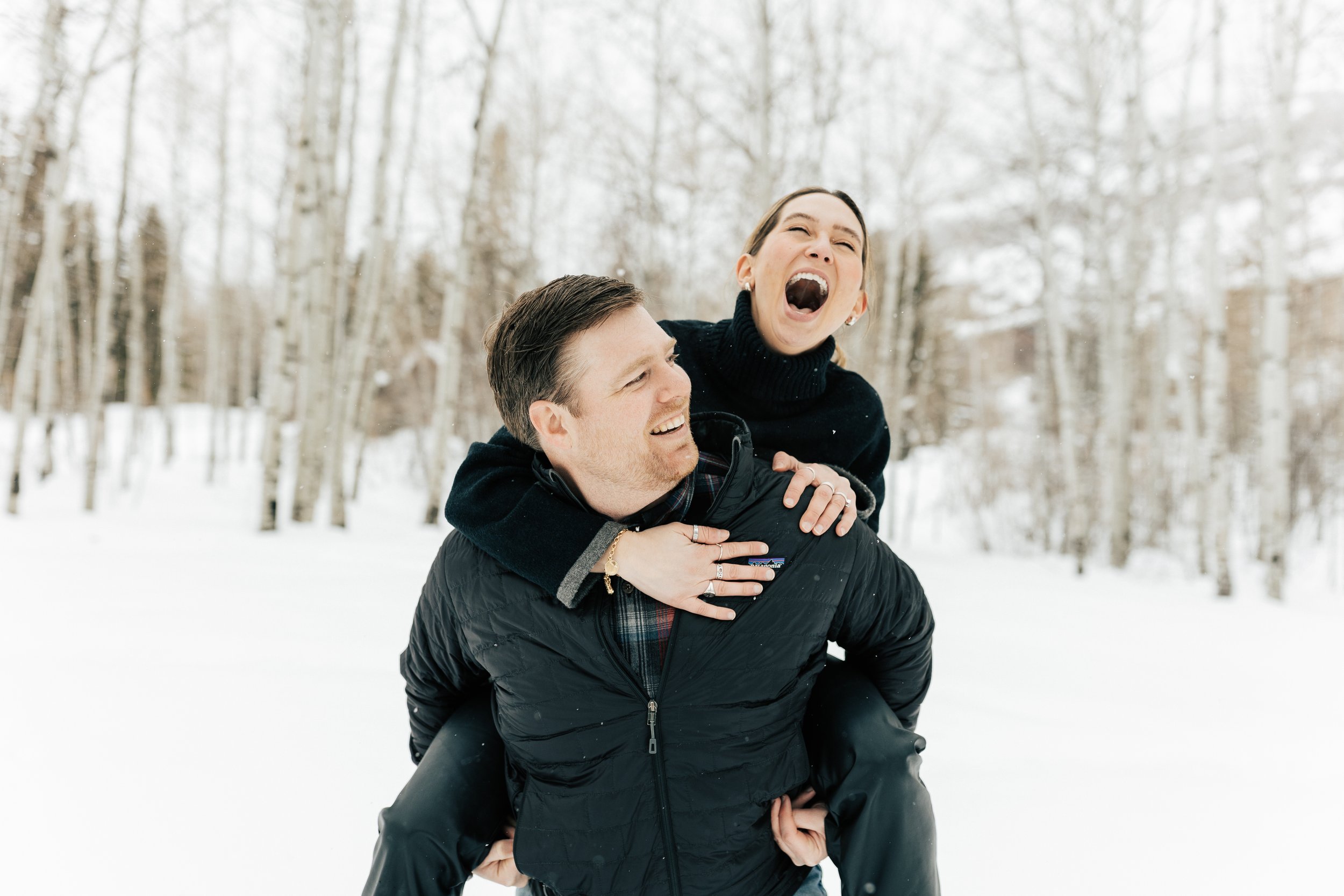  Newly engaged couple laughing piggyback ride. Winter engagement session in Park City, Utah. Boyfriend surprises girlfriend with wedding proposal during a snowy photoshoot. Man proposes to girlfriend. Outfit inspo. #parkcity #engagements #engagements