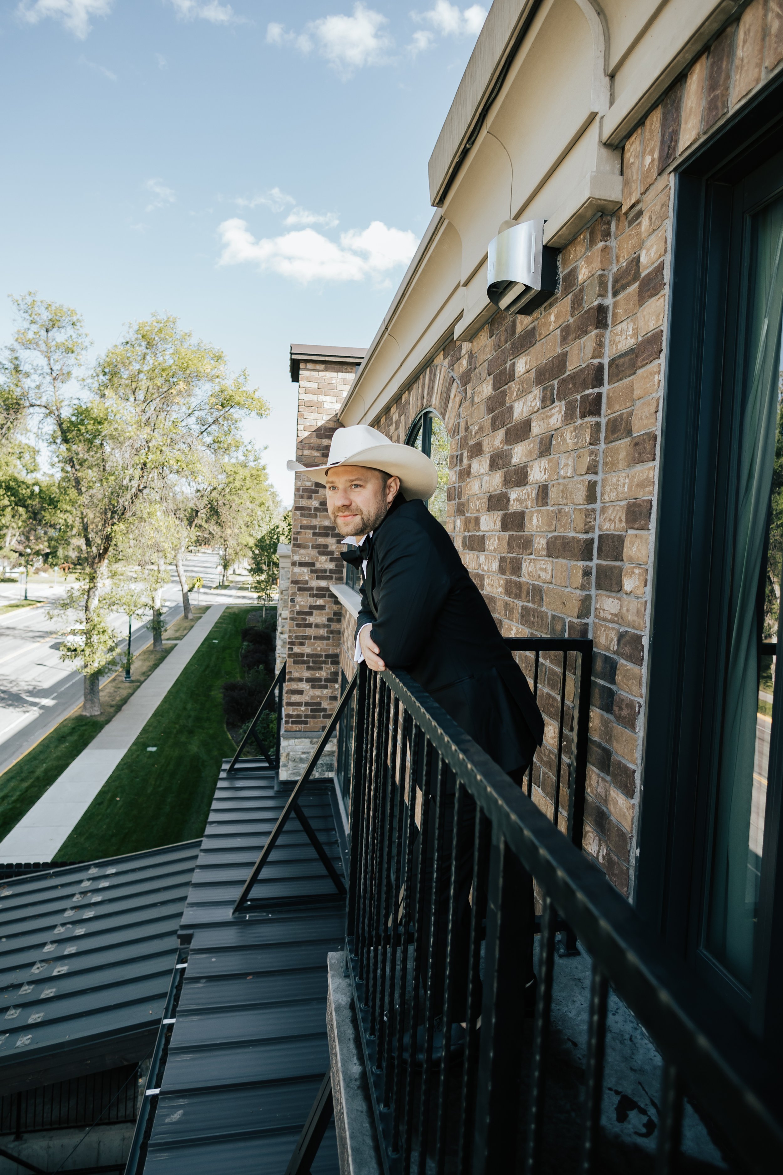  Groom on hotel balcony overlooking the city before the wedding ceremony begins in Whitefish, Montana. Groom in cowboy hat. #groom #weddingphotography 
