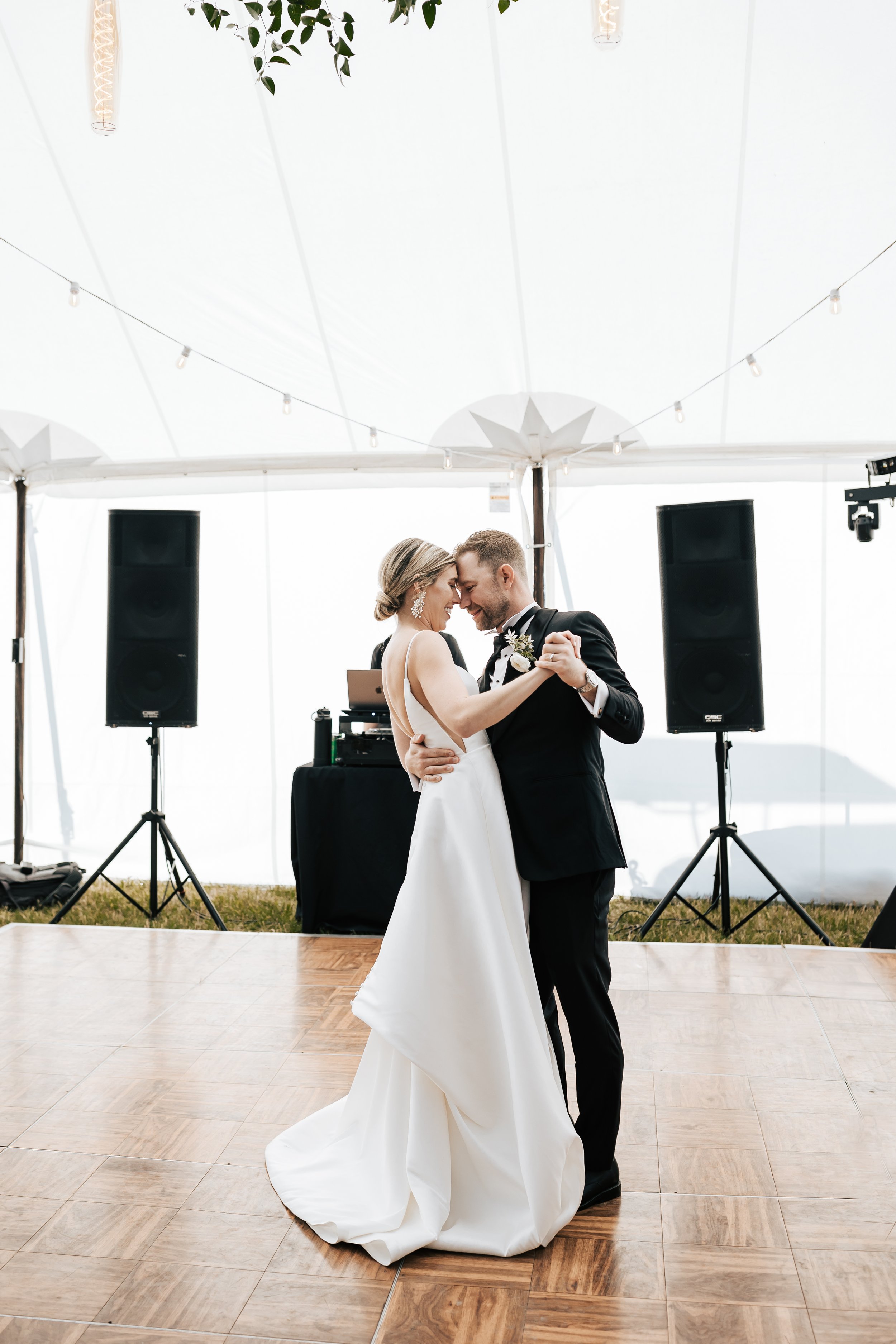  Bride and groom first dance. Bride and groom smile at wedding in the forest in Whitefish, Montana. Wedding inspo. Bride is wearing gorgeous large white earrings with a strappy wedding dress and veil and groom is wearing a black suit and bowtie. #mon