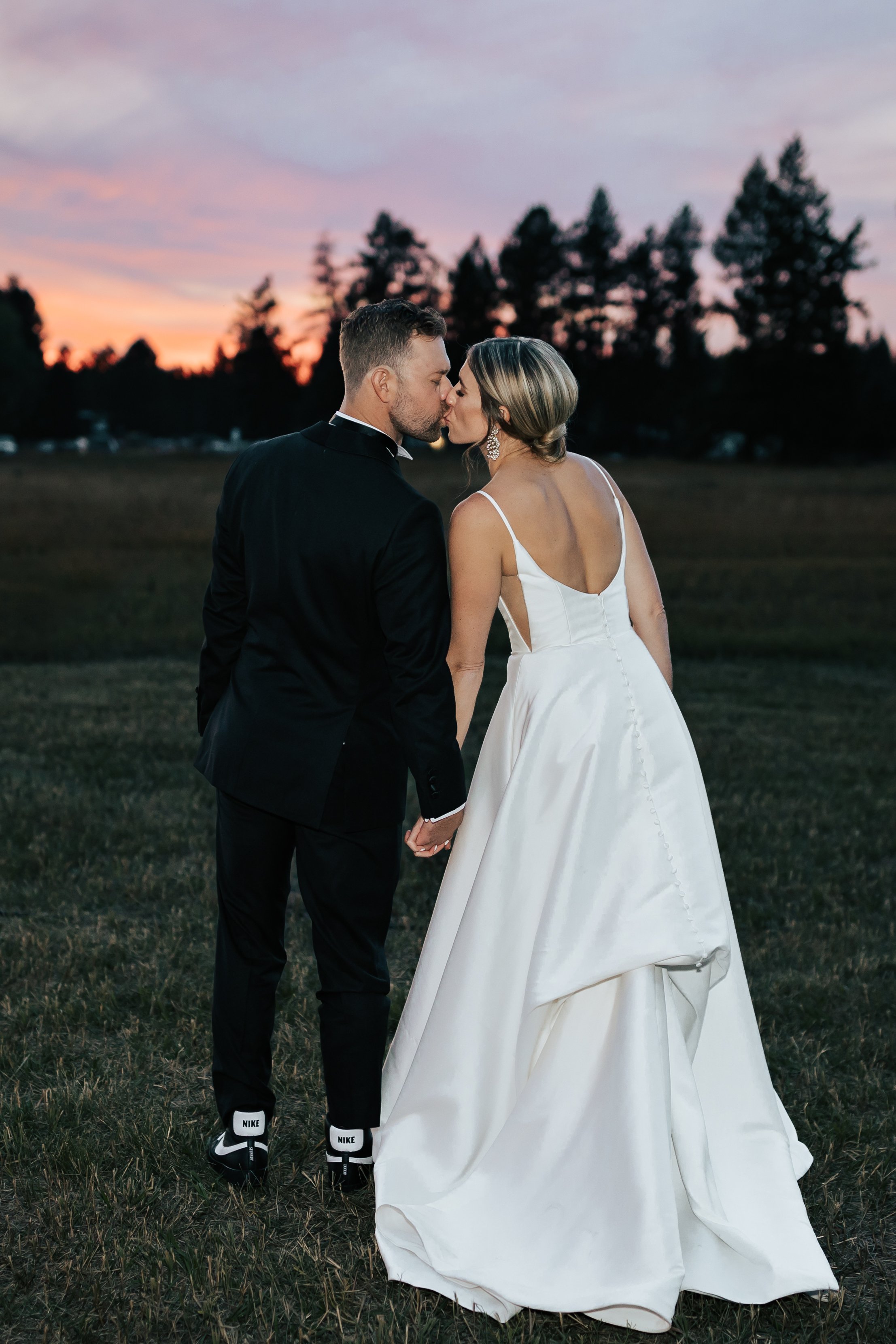  Bride and groom wedding sunset portraits surrounded by beautiful flowers and pine trees. Bride and groom smile at wedding in the forest in Whitefish, Montana. Wedding inspo. Bride is wearing gorgeous large white earrings with a strappy wedding dress