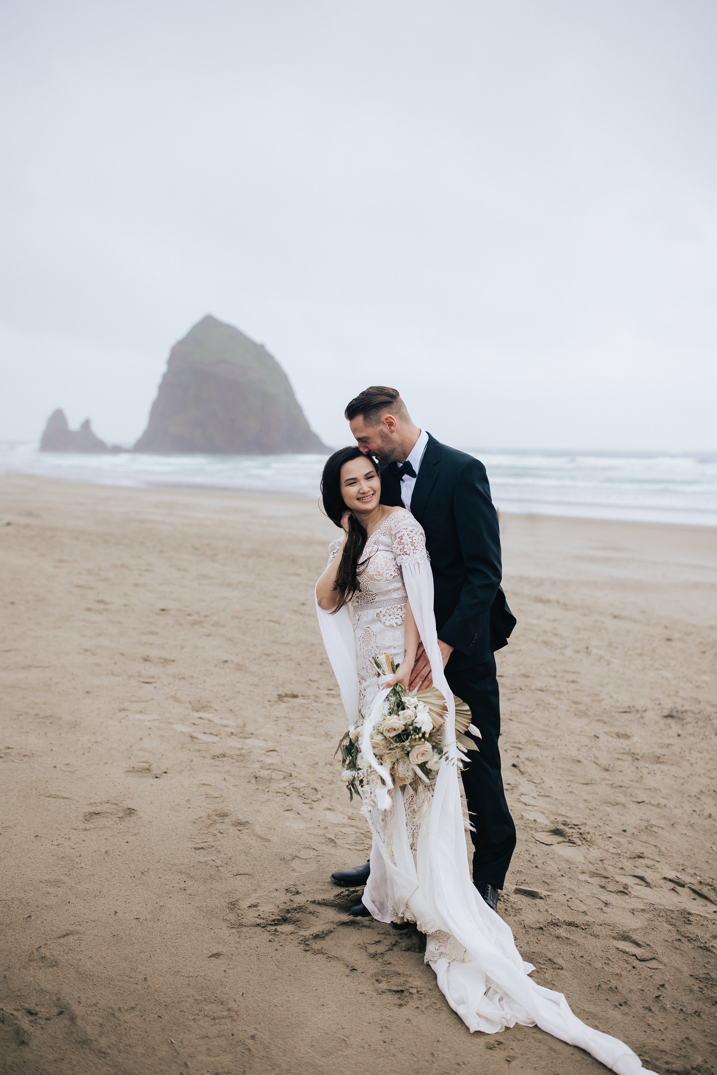  Bride and groom stand together on cannon beach in Oregon elopement photographer emily jenkins photo beach wedding overcast elopement beach sand photos pnw pacific northwest wedding photographer seaside oregon #pnw #pnwwedding #pnwelopement #cannonbe