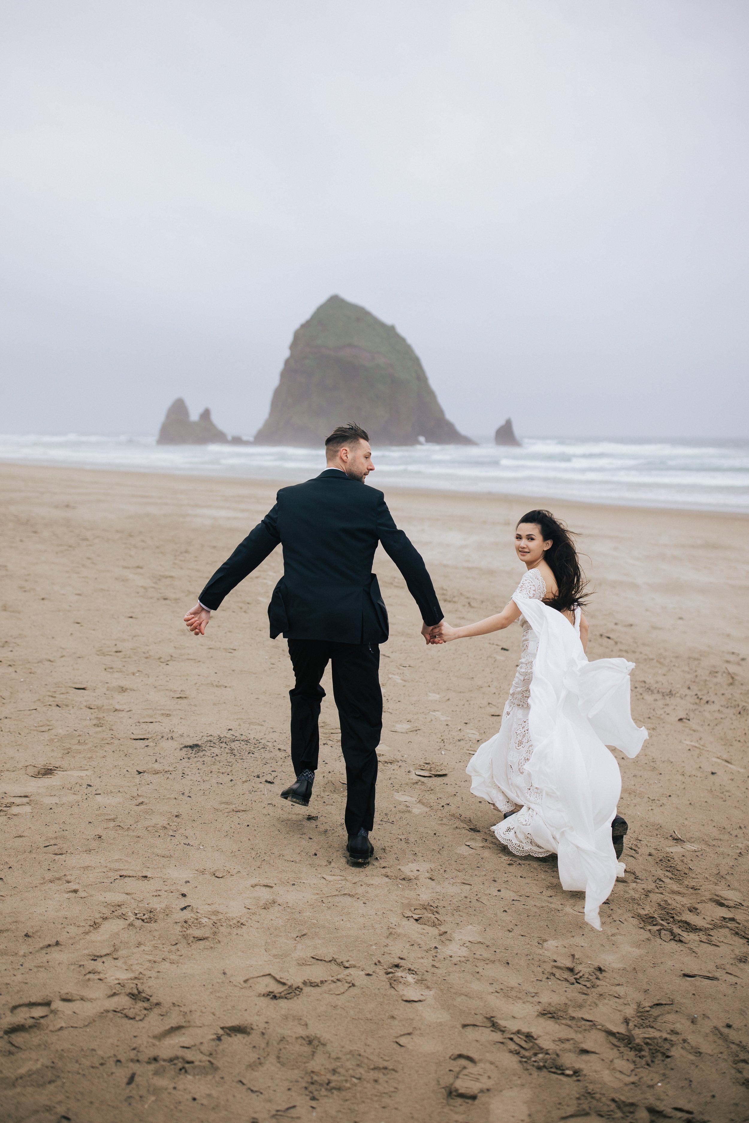  bride and groom running away elopement beach photographer cannon beach elopement boho wedding style how to elope to cannon beach in pacific northwest seaside oregon emily jenkins photo pnw elopement photographer available to travel #pnw #pnwwedding 