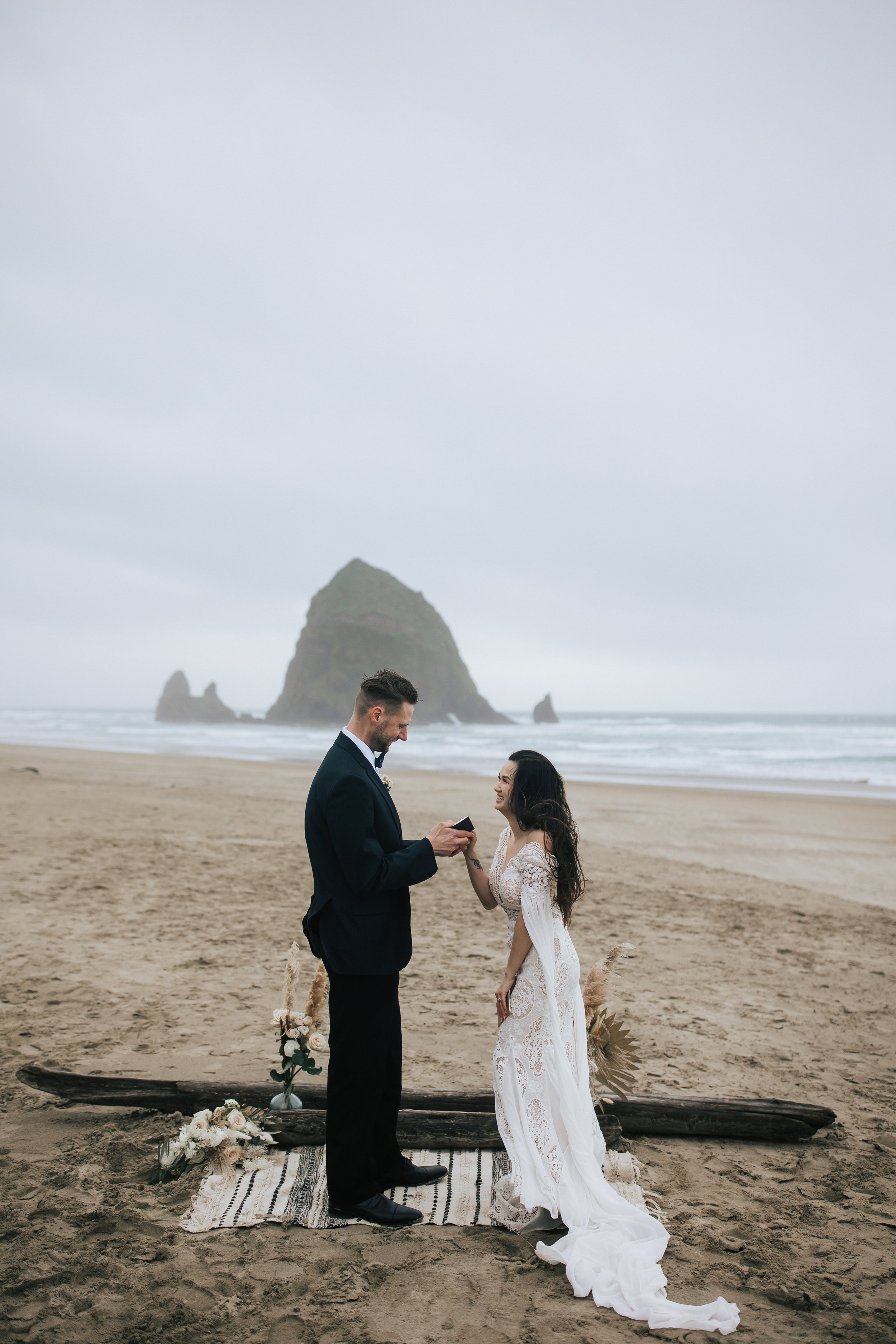  Groom reads vows to boho bride during beach wedding oceanside elopement in cannon beach photographed by pacific northwest elopement photographer emily jenkins photo seaside wedding pnw brides #pnw #pnwwedding #pnwelopement #cannonbeach #cannonbeache