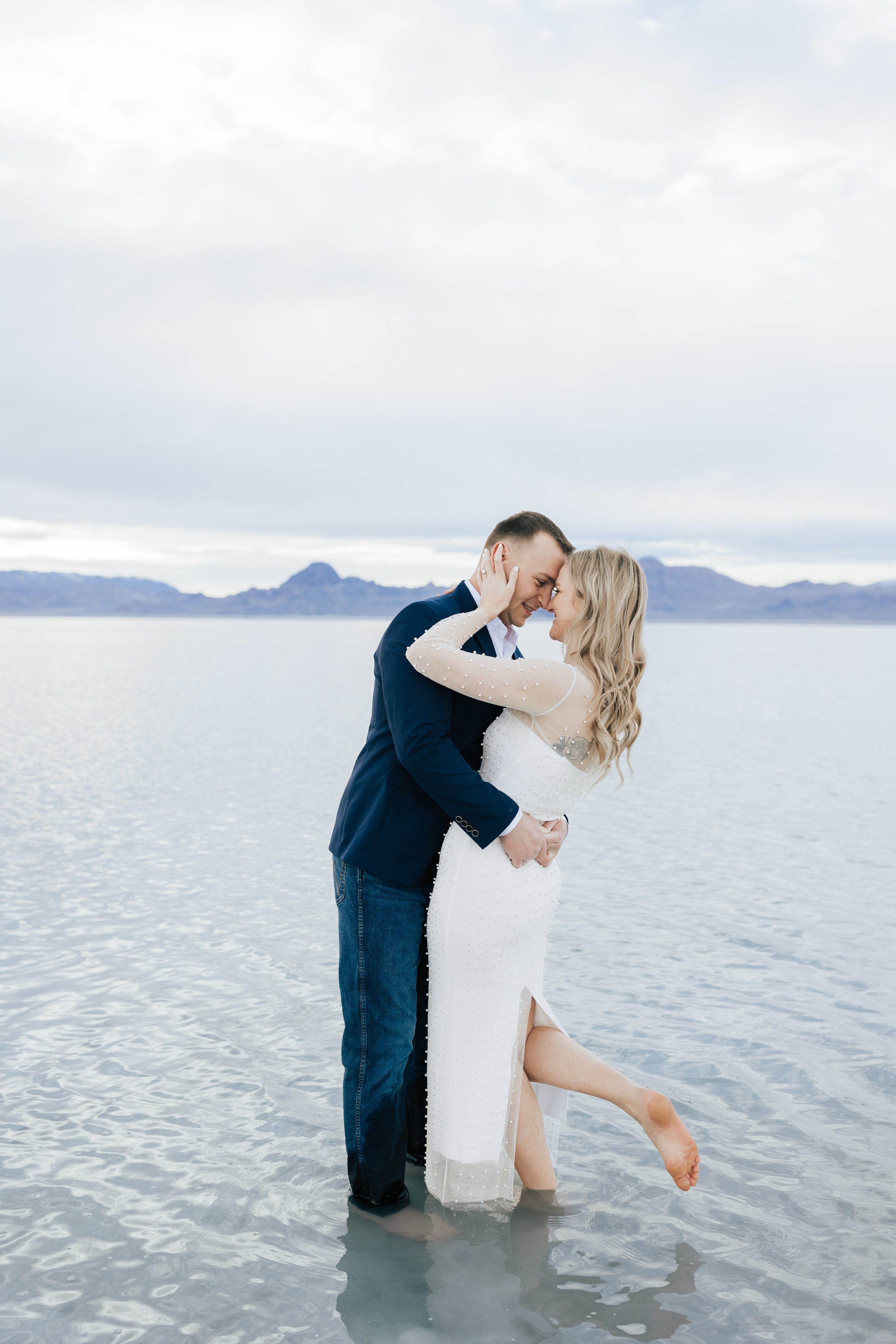  An engaged couple kissing with the woman's leg popped up by Emily Jenkins Photography on a lake in Utah. kissing couple water engagements Utah Engagements #EmilyJenkinsPhotography #EmilyJenkinsEngagements #BonnevilleSaltFlats #SaltFlatEngagements #U