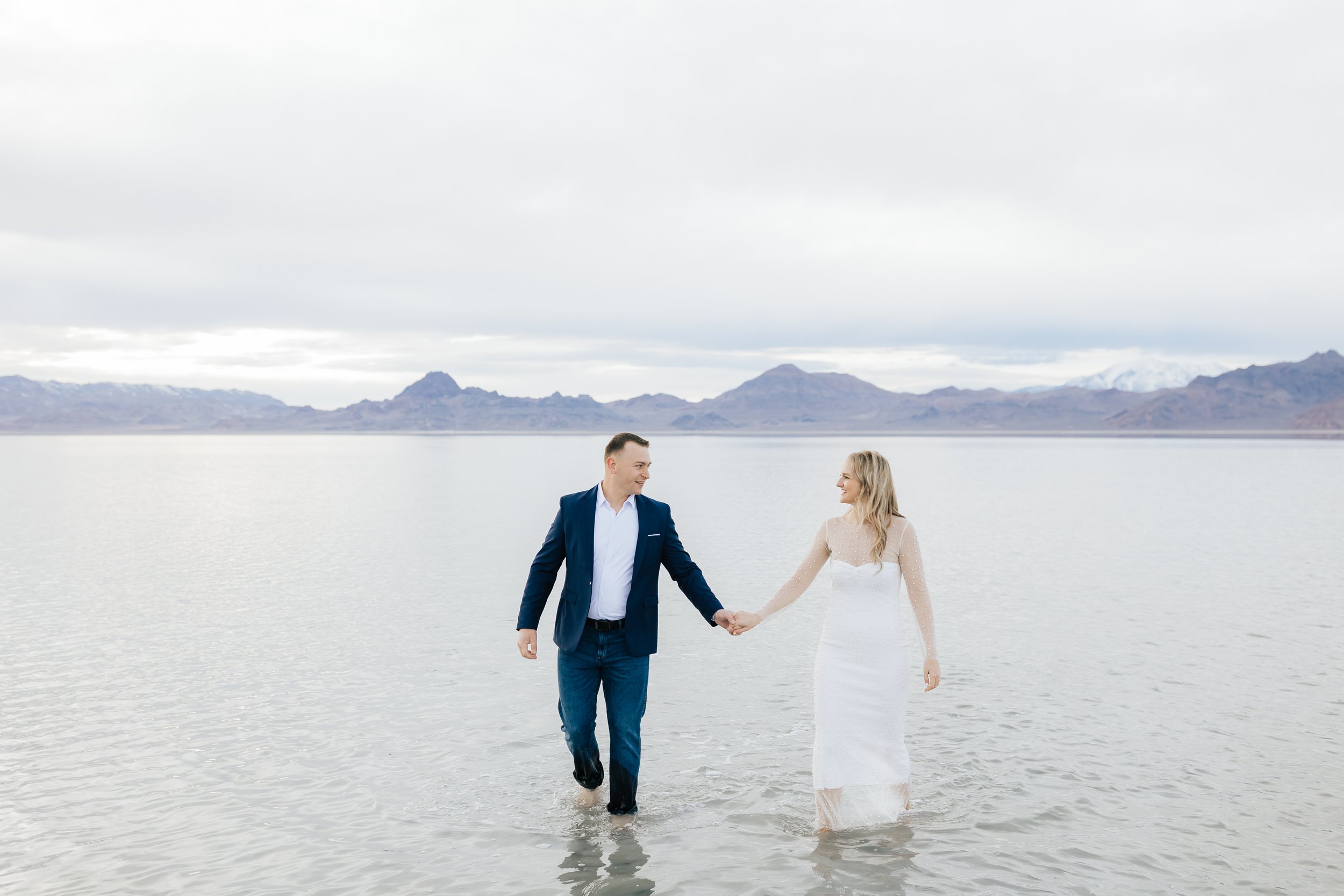  Soon-to-be husband and wife hold hands walking at Bonneville Salt Flats in the springtime by Emily Jenkins Photography. summer engagements in UT summer outfits #EmilyJenkinsPhotography #EmilyJenkinsEngagements #BonnevilleSaltFlats #SaltFlatEngagemen
