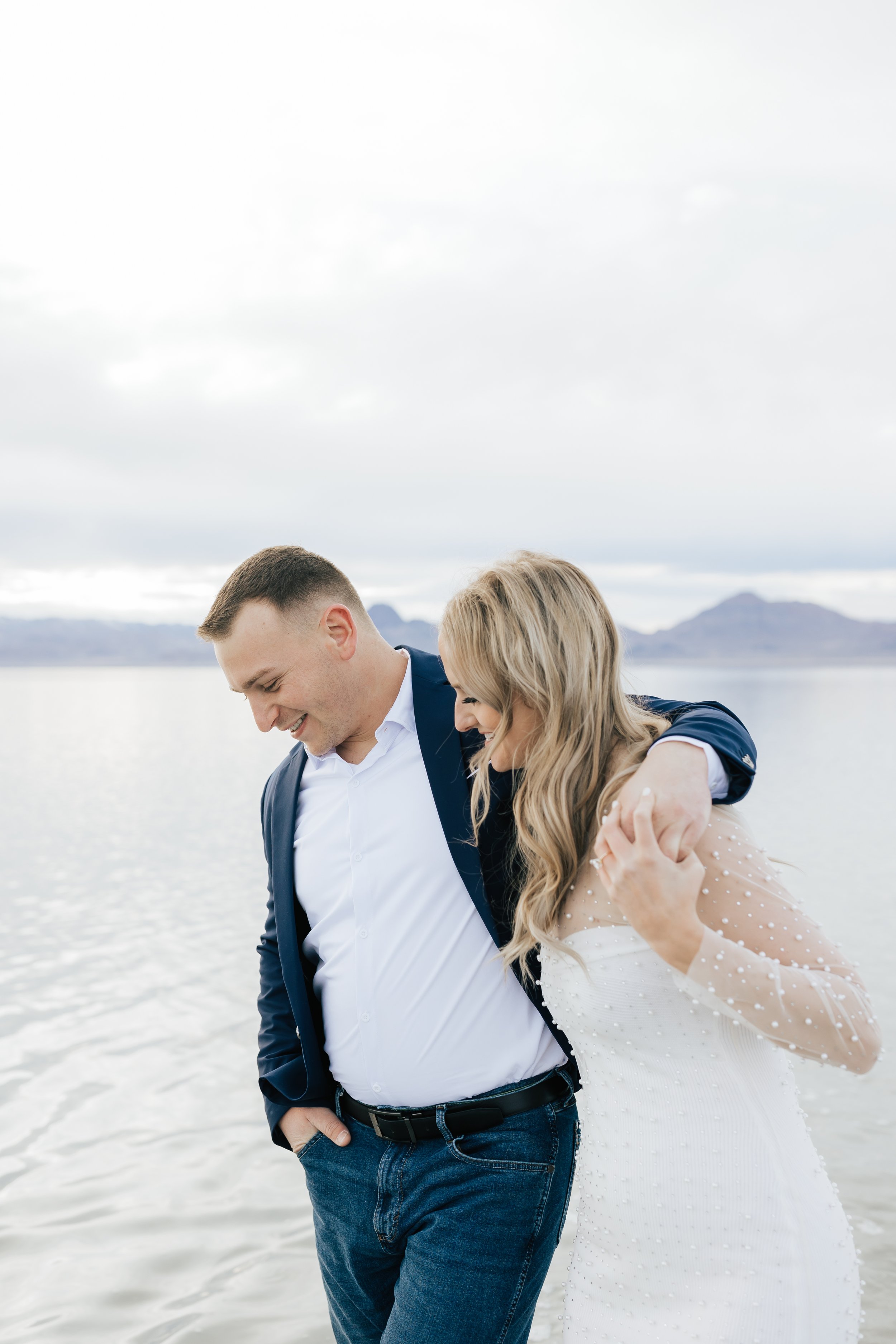  A man in a navy suit jacket and white shirt wraps his arm around his girlfriend and walks in the Bonneville Salt Flats by Emily Jenkins Photography. engagement men outfit ideas dress and suit outfit for engagements #EmilyJenkinsPhotography #EmilyJen