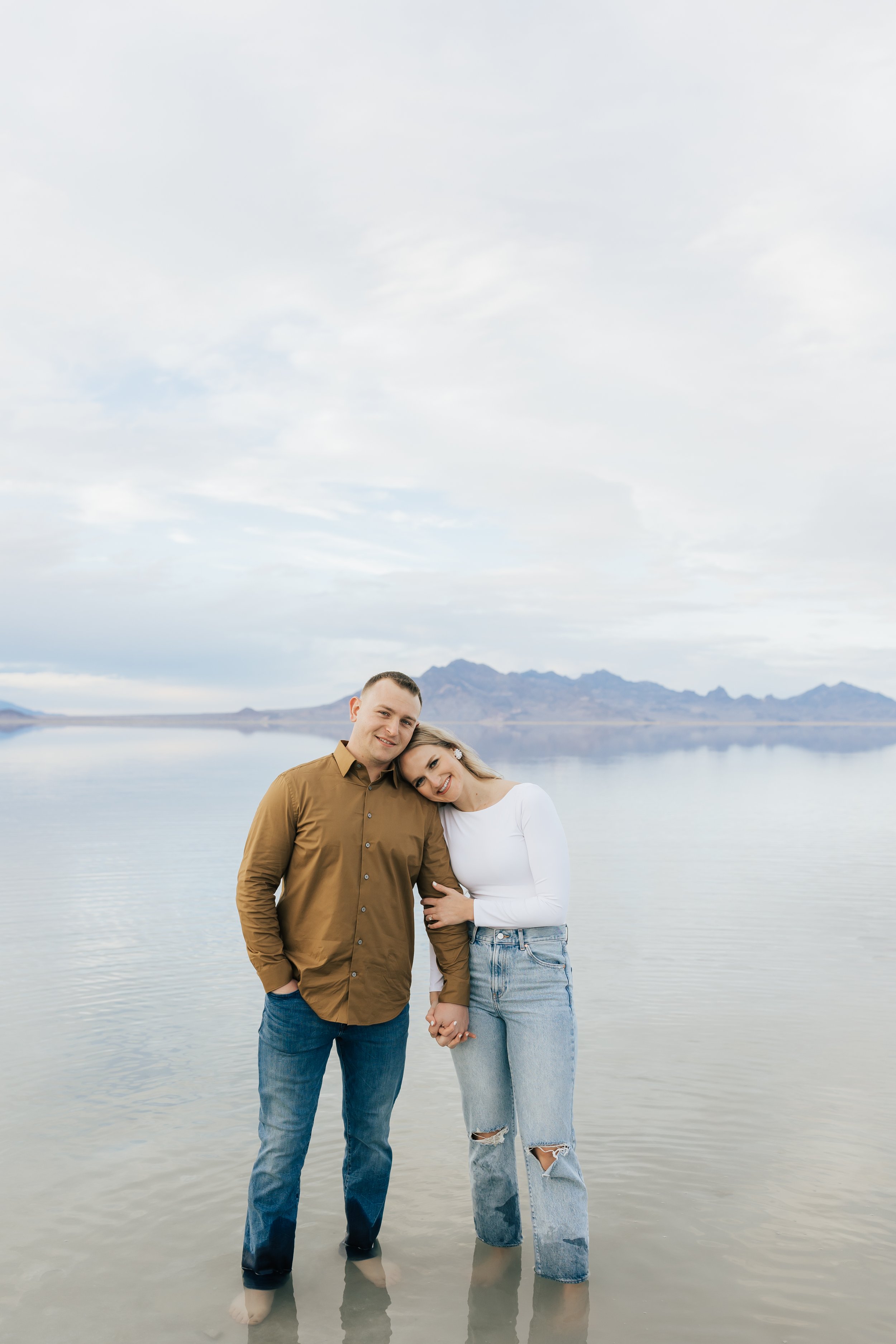  A woman leans her head on her boyfriend's shoulder holding his arm by Emily Jenkins Photography. tan shirt camel colored men shirt jeans and shirt  #EmilyJenkinsPhotography #EmilyJenkinsEngagements #BonnevilleSaltFlats #SaltFlatEngagements #UtahEnga