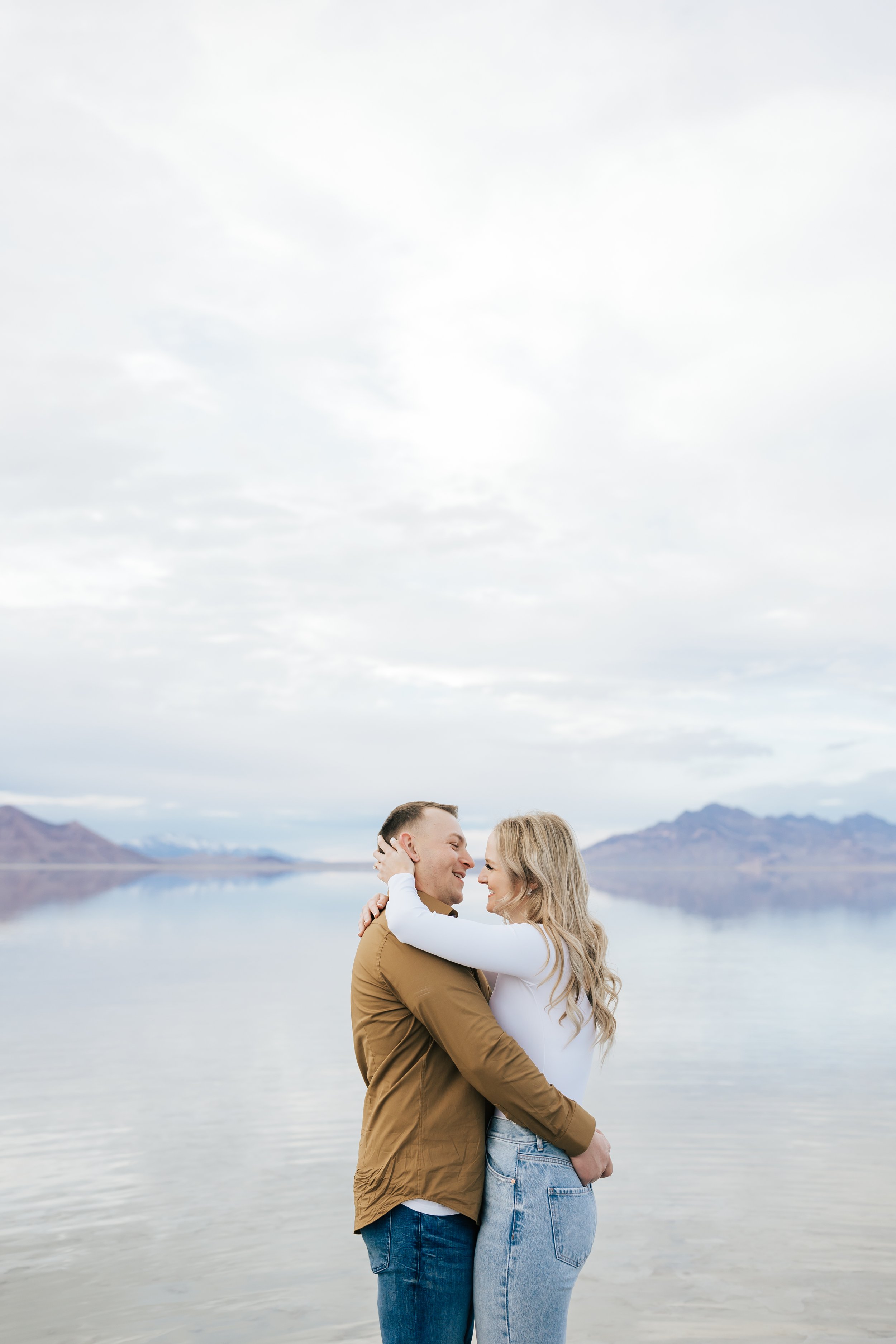  Husband and wife hold each other tight while standing in the middle of Bonneville Salt Flats by Emily Jenkins Photography. summer spring engagement locations neutral locations Utah #EmilyJenkinsPhotography #EmilyJenkinsEngagements #BonnevilleSaltFla