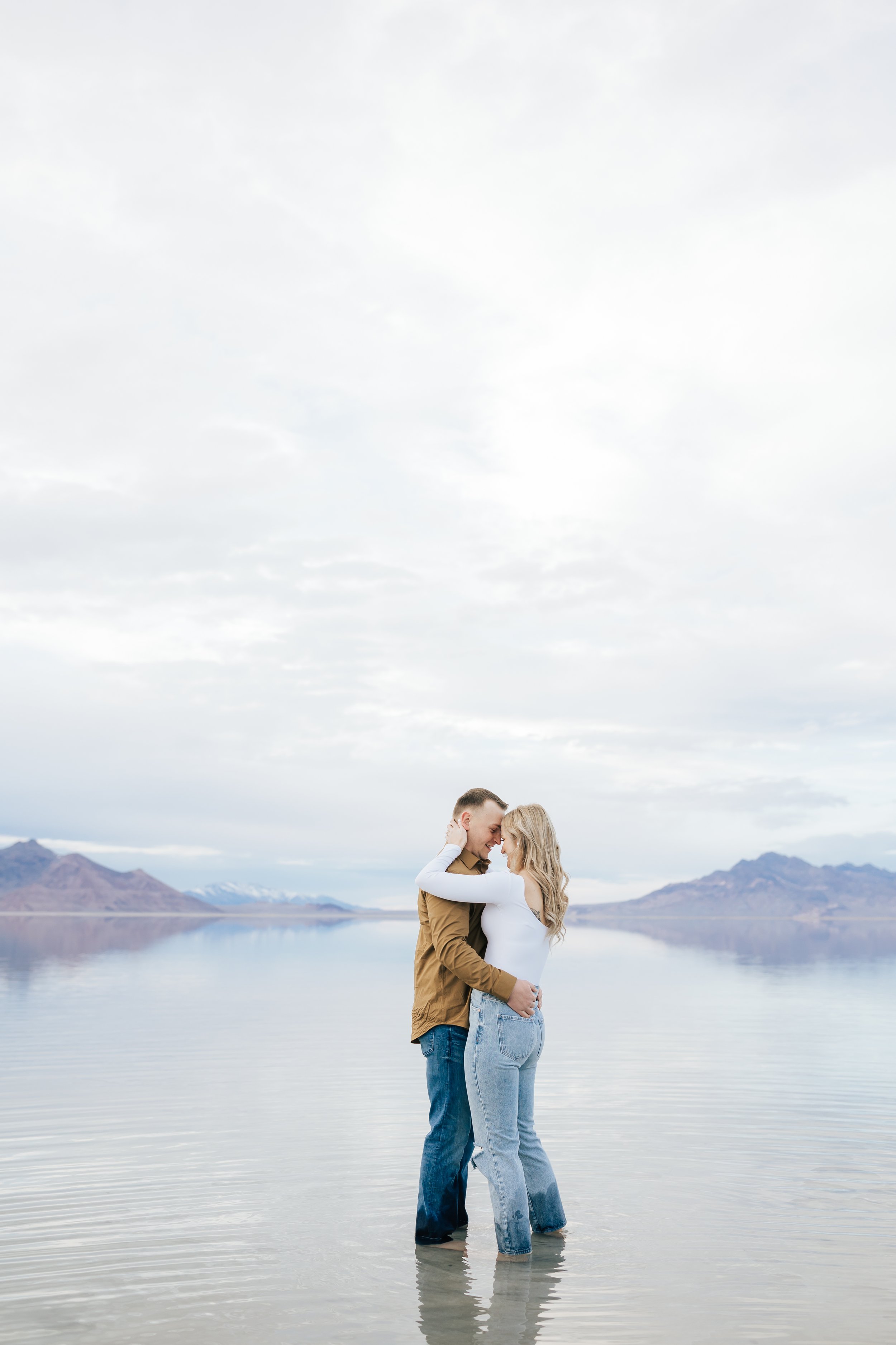  At the Bonneville Salt Flats, a couple stands in ankle-deep water in their jeans and embrace, Emily Jenkins Photography. engagement inspiration UT dream engagement portraits #EmilyJenkinsPhotography #EmilyJenkinsEngagements #BonnevilleSaltFlats #Sal