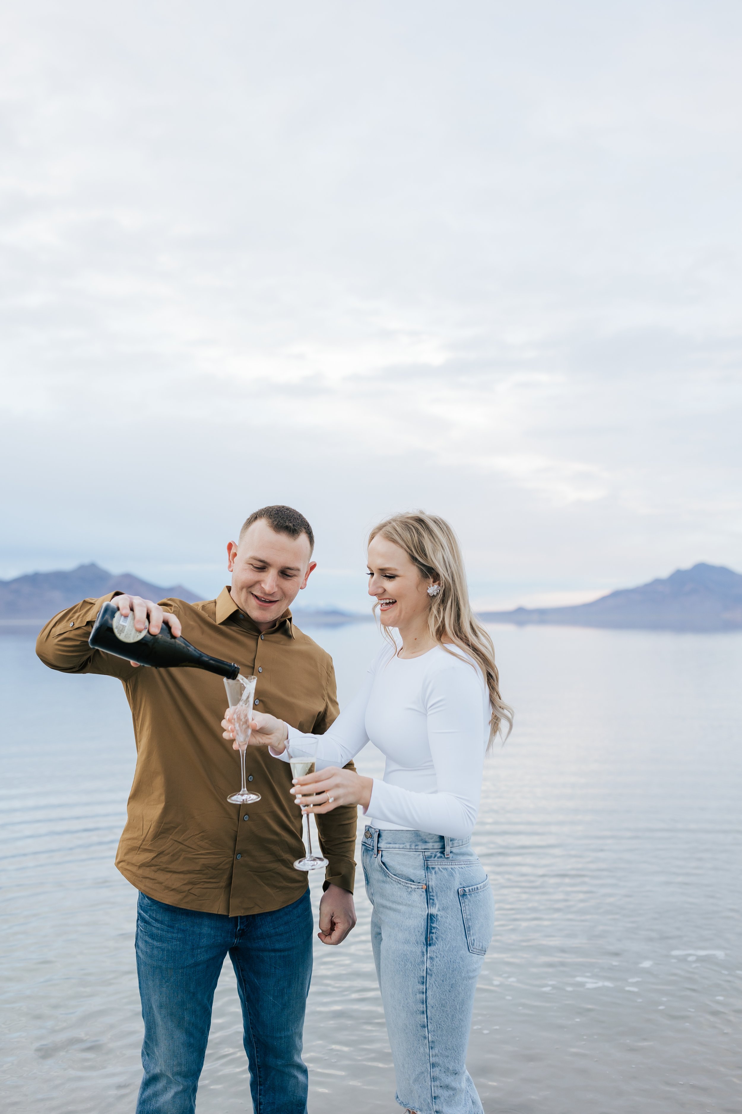  A couple toast to their engagement with champagne in Northern Utah captured by Emily Jenkins Photography. champagne engagement toast pouring a toast #EmilyJenkinsPhotography #EmilyJenkinsEngagements #BonnevilleSaltFlats #SaltFlatEngagements #UtahEng