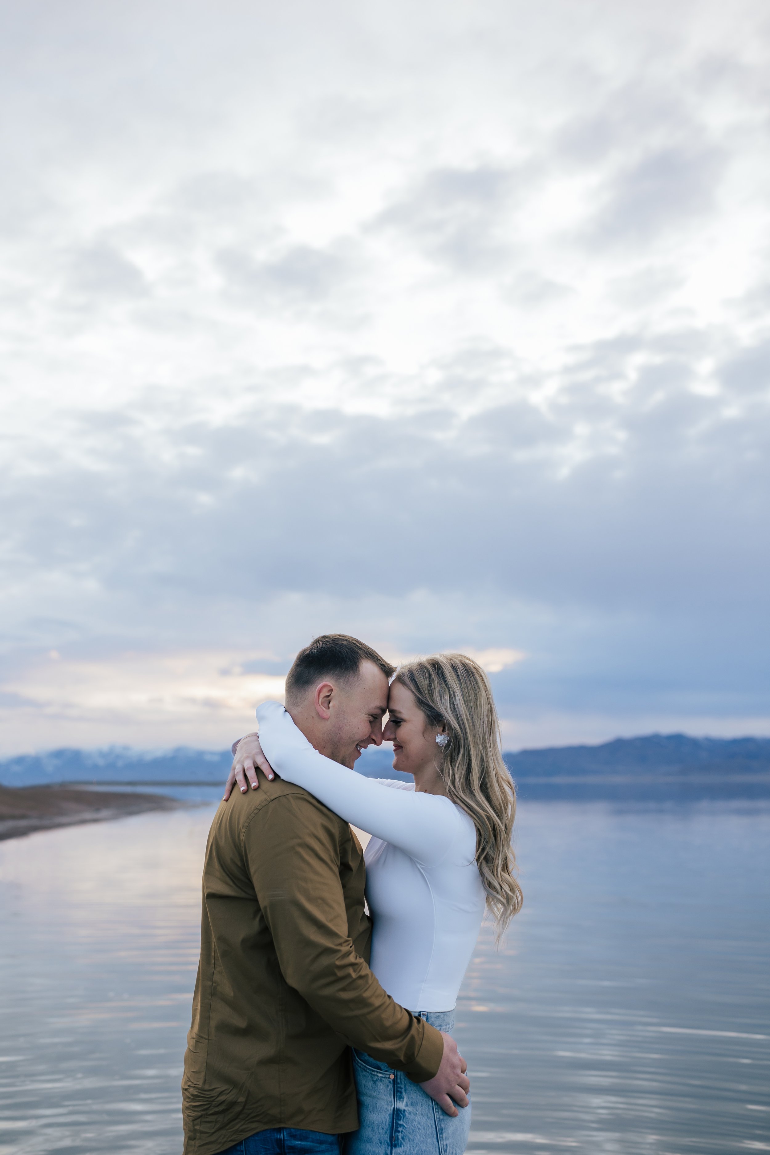  At dusk at the Bonneville Salt Flats, a couple embraces while standing in the water taken by Emily Jenkins photography. dusk engagements couple style ideas engagement casual outfits #EmilyJenkinsPhotography #EmilyJenkinsEngagements #BonnevilleSaltFl