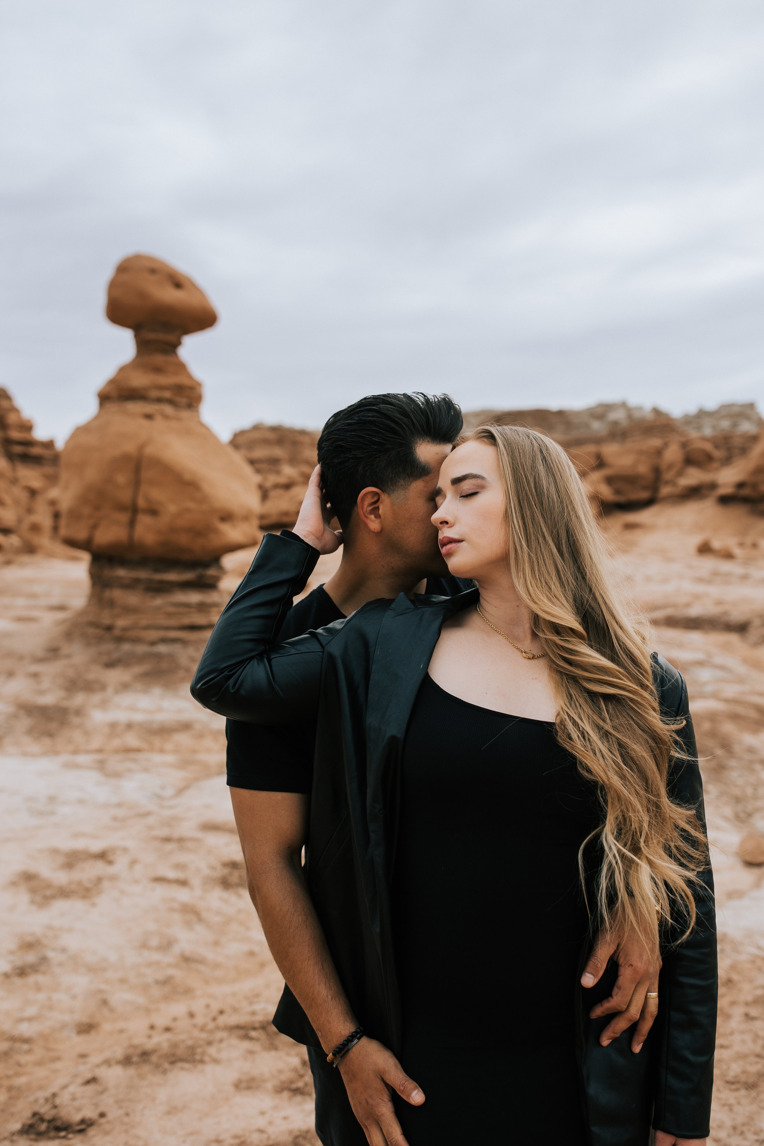 A woman leans into her fiance as he snuggles her in Hanksville, Utah captured by Emily Jenkins Photography. black outfits red rock engagements Hanksville Engagements #EmilyJenkinsPhotography #EmilyJenkinsEngagements #HanksvillePhotography #GoblinVal