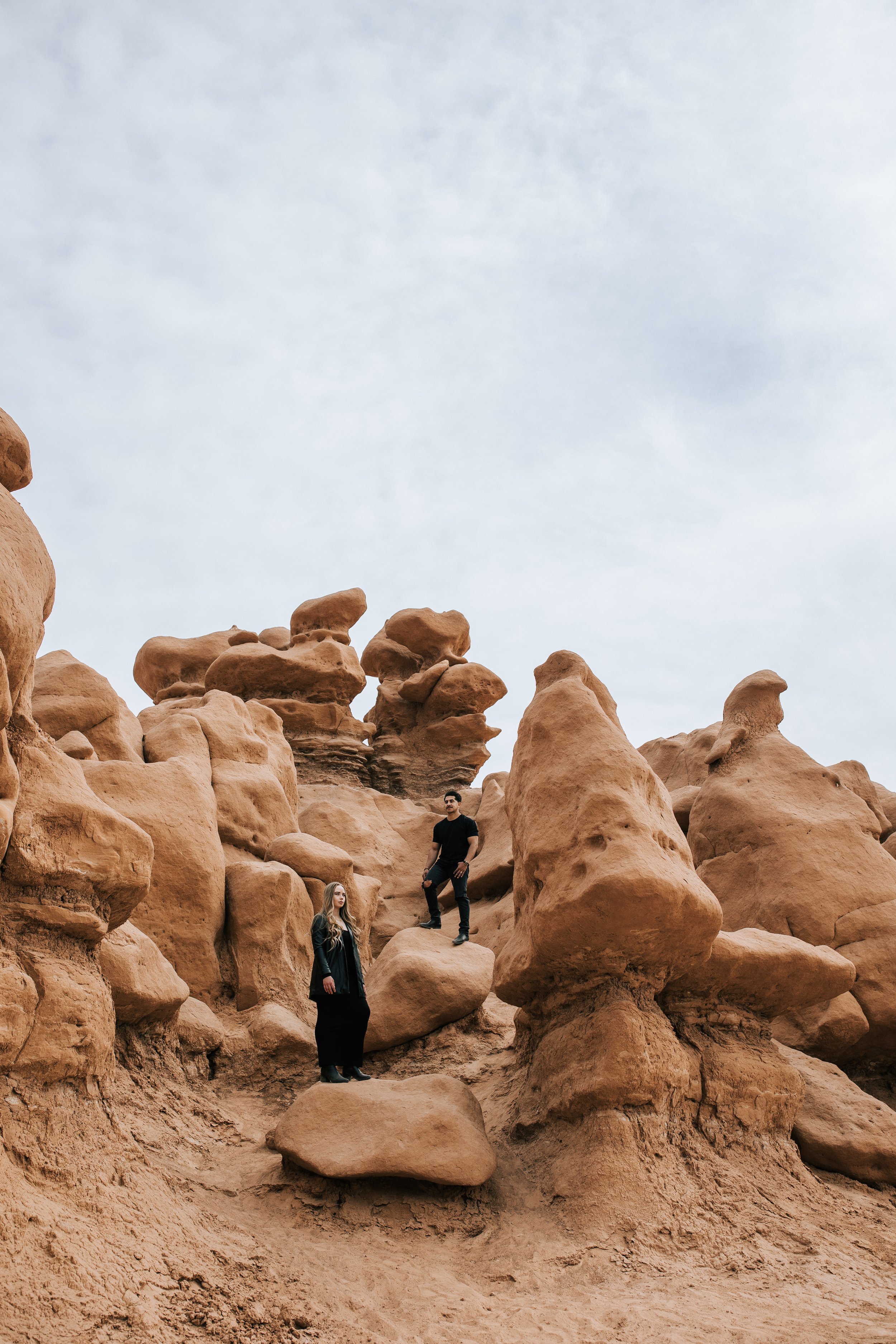 An engaged couple poses in the red rocks in Goblin Valley during an engagement session with Emily Jenkins Photography. black engagement outfits granola location engagements #EmilyJenkinsPhotography #EmilyJenkinsEngagements #HanksvillePhotography #Go