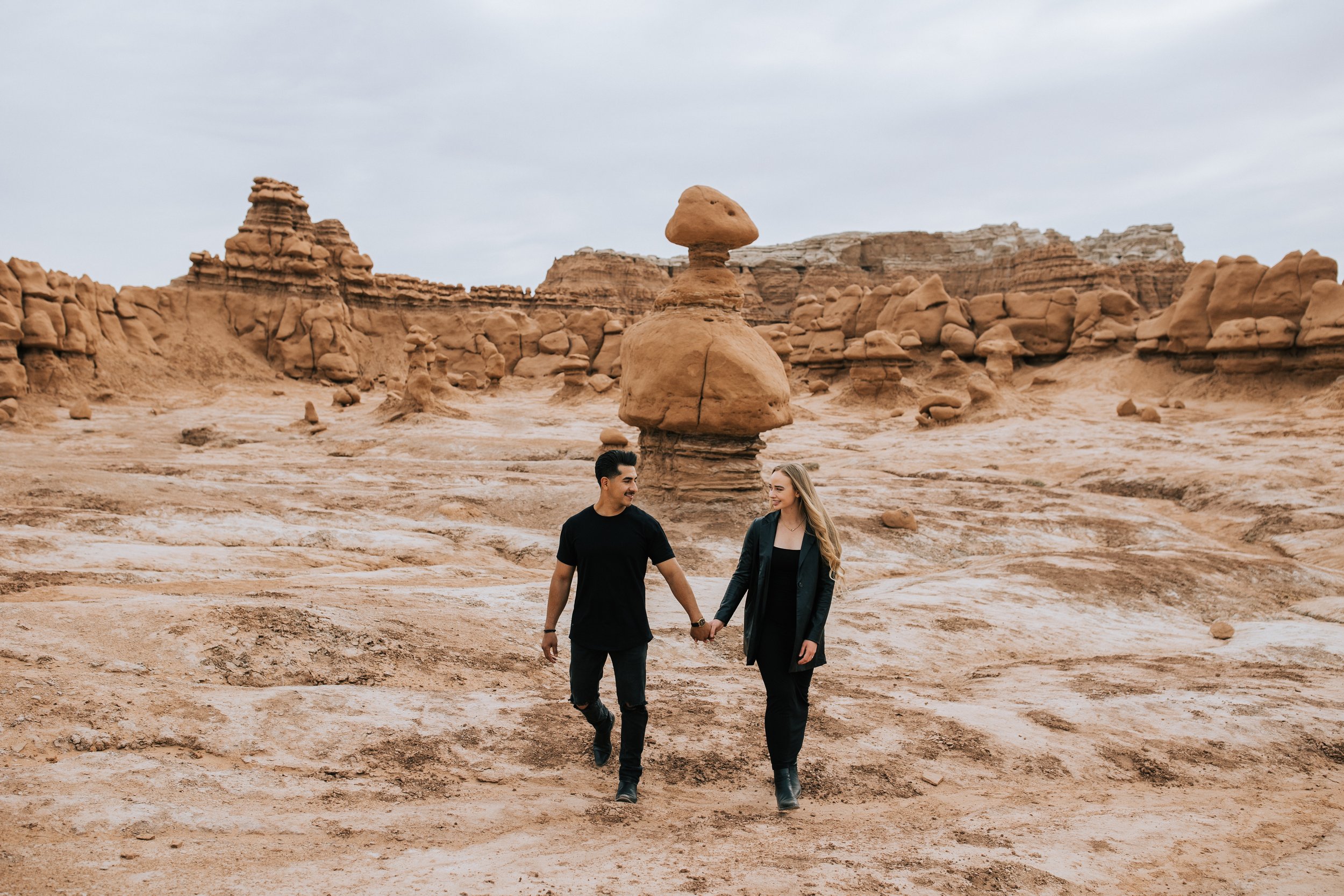  Standing in a unique landscape of red rock a couple hold hands looking at each other by Emily Jenkins Photography. unique engagements bold outdoors engagement locations #EmilyJenkinsPhotography #EmilyJenkinsEngagements #HanksvillePhotography #Goblin