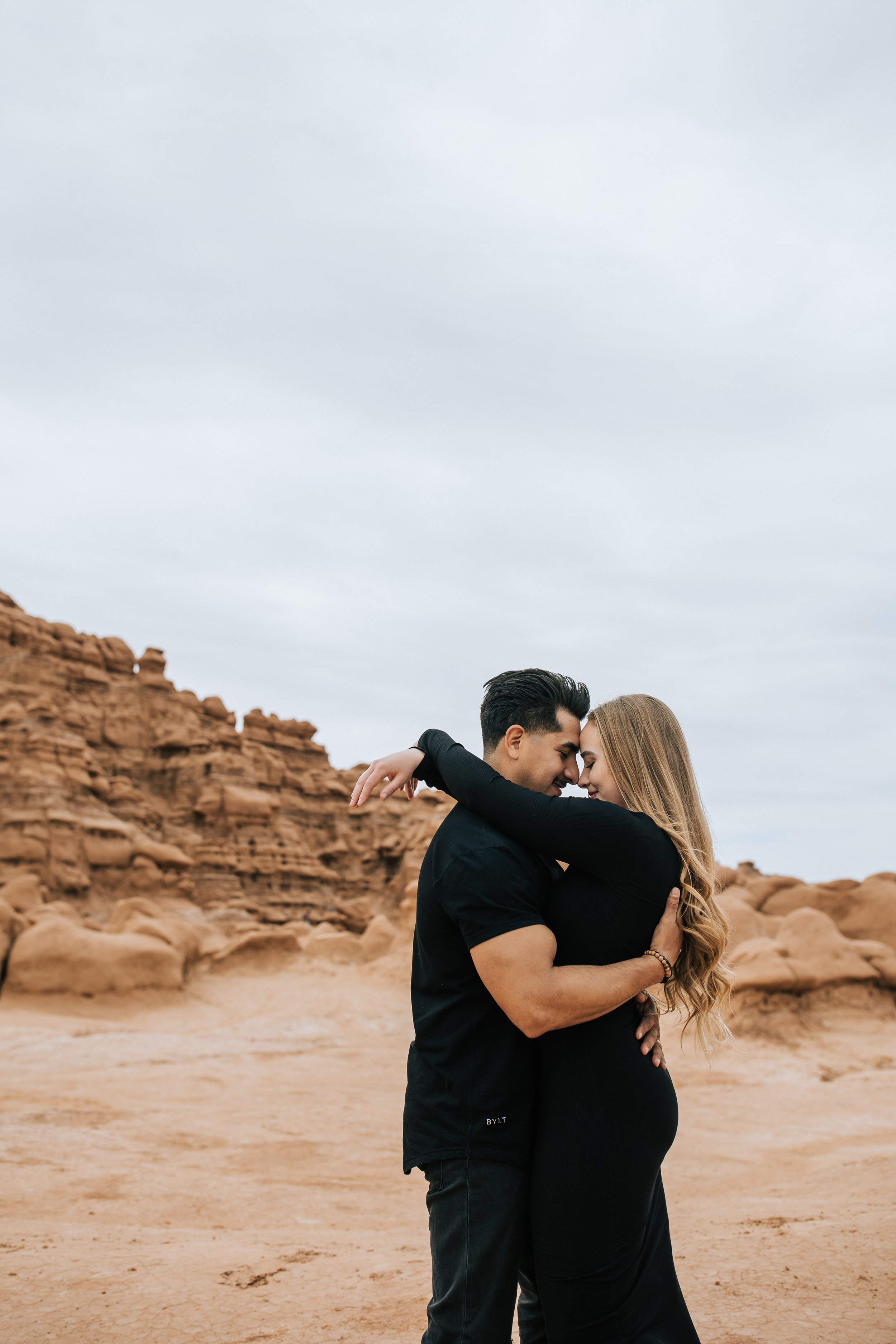  In Goblin Valley Emily Jenkins Photography captures a newly engaged couple kissing in the middle of a red rock valley. kissing engagements stylized engagement travel elopement locations Utah #EmilyJenkinsPhotography #EmilyJenkinsEngagements #Hanksvi