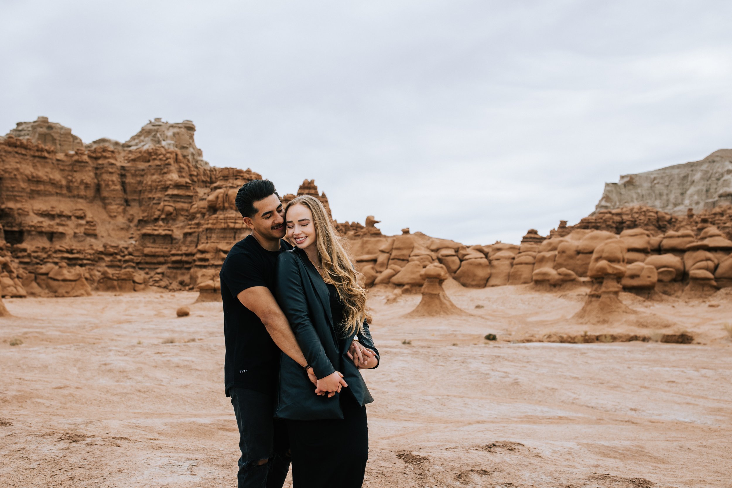  Soon-to-be married couple snuggles together in a picturesque location in Hanksville, Utah by Emily Jenkins Photography. Southern Utah hiking couple outdoorsy engagements #EmilyJenkinsPhotography #EmilyJenkinsEngagements #HanksvillePhotography #Gobli