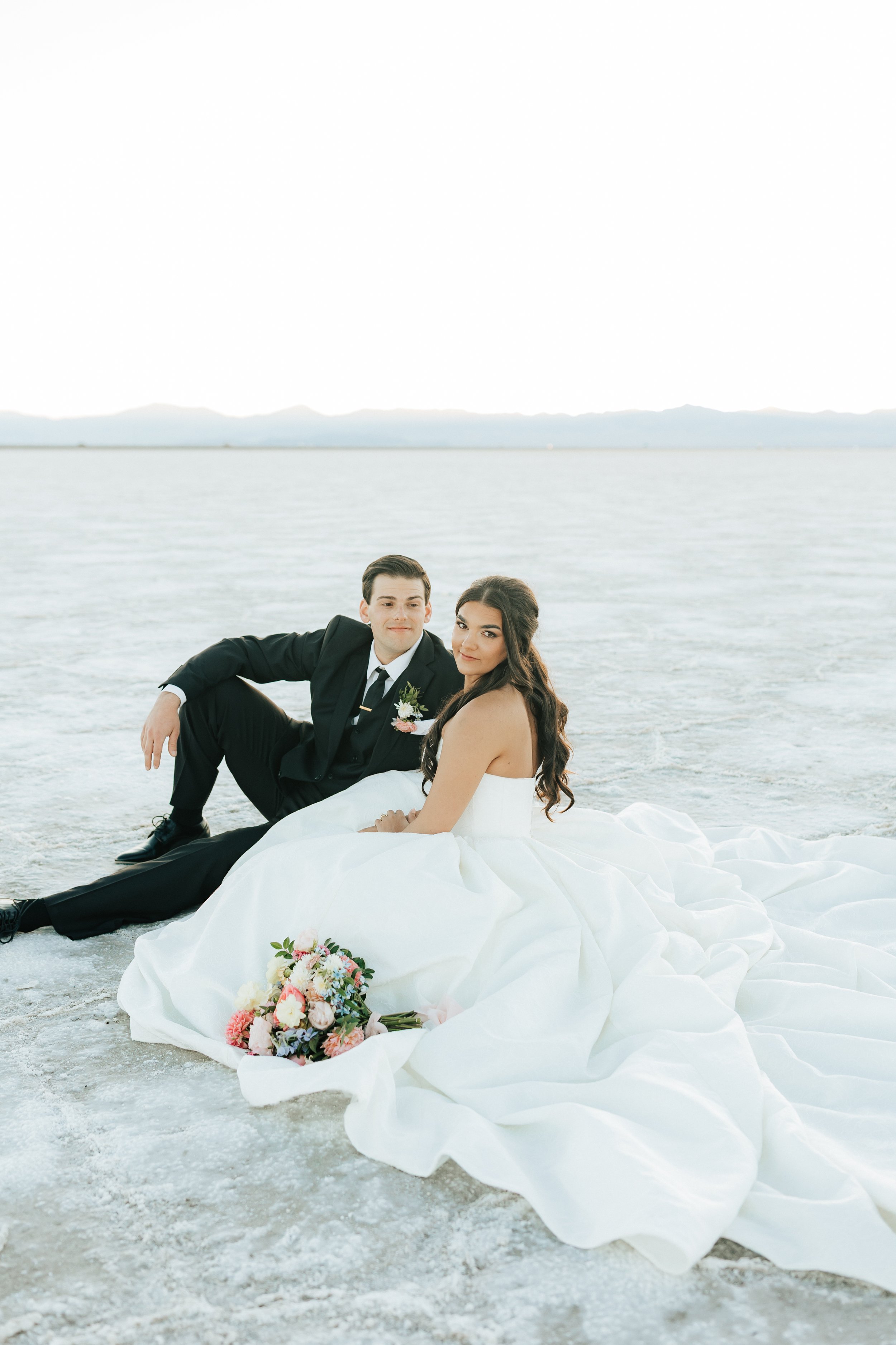  Bride sits in her beautiful ball gown wedding dress with groom after their wedding ceremony at the Salt Flats near Salt Lake City, Utah 
