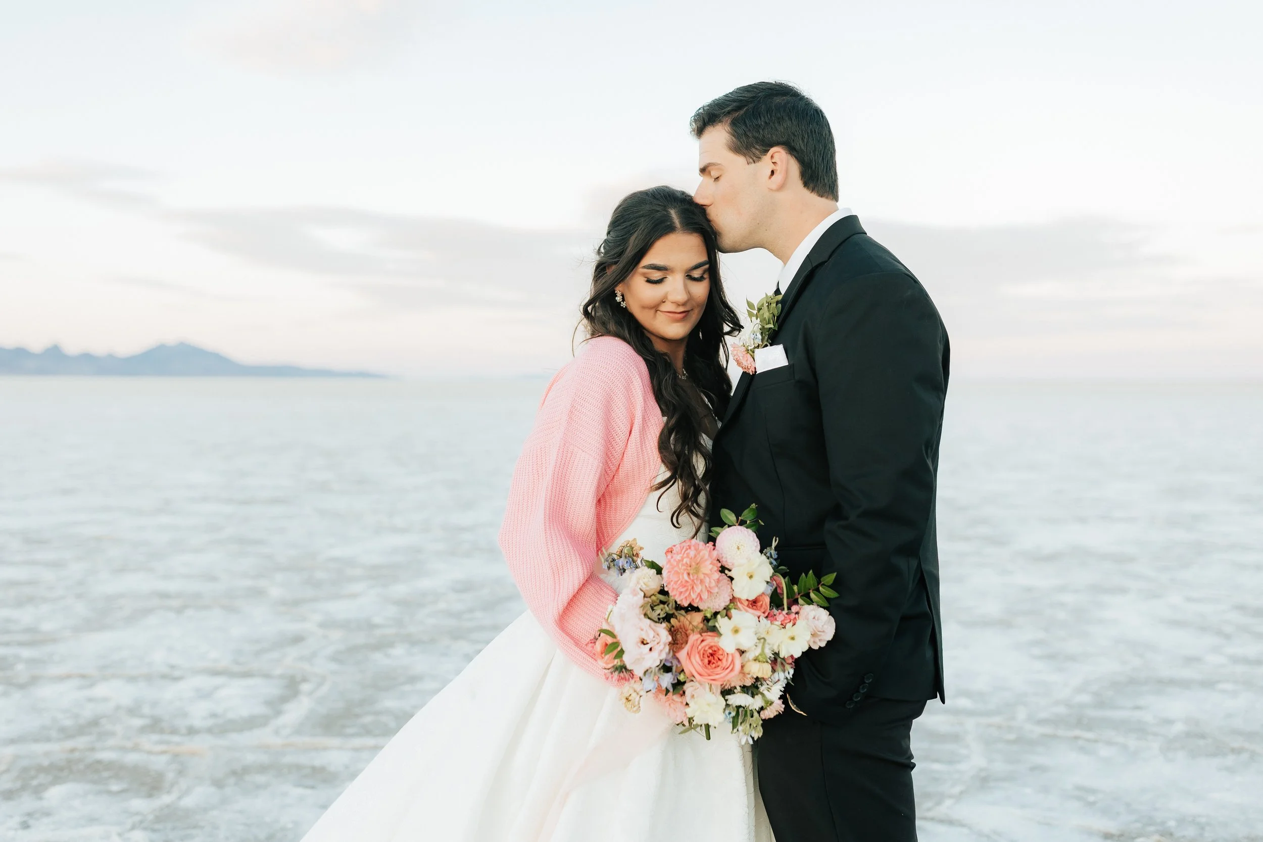  Couples poses in wedding dress and wedding suit with beautiful pink flowers at the salt flats near Salt Lake City, Utah 