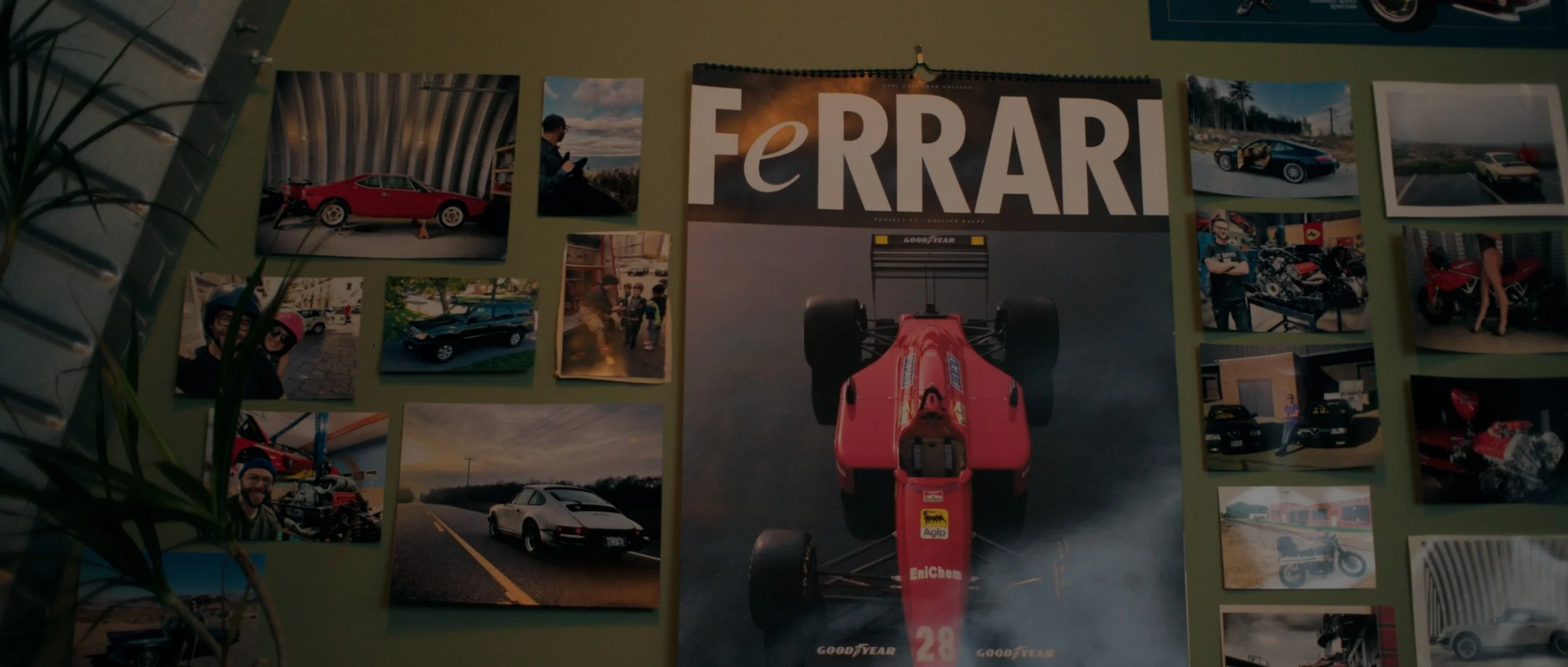 Collection of photographs on a green wall, centered around a large Ferrari poster featuring a red Formula 1 car, with various images of vintage and modern cars, people, and racing scenes surrounding it.