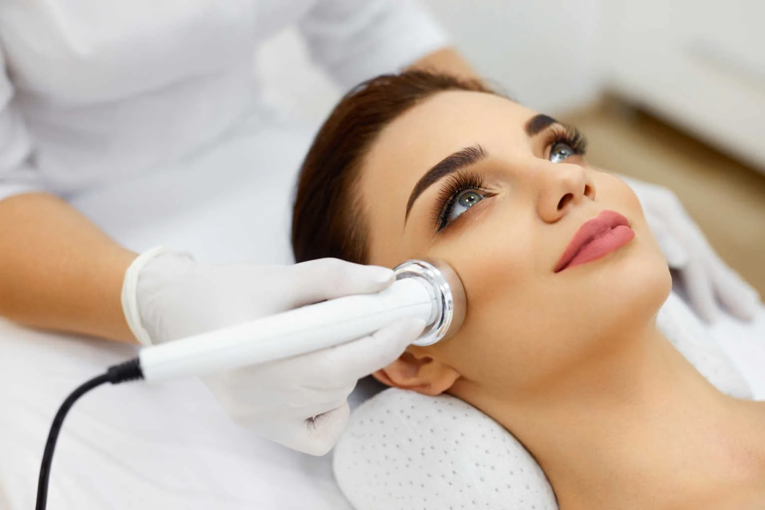 Una donna riceve un trattamento estetico al viso con un apparecchio medico, mentre è sdraiata su un lettino.