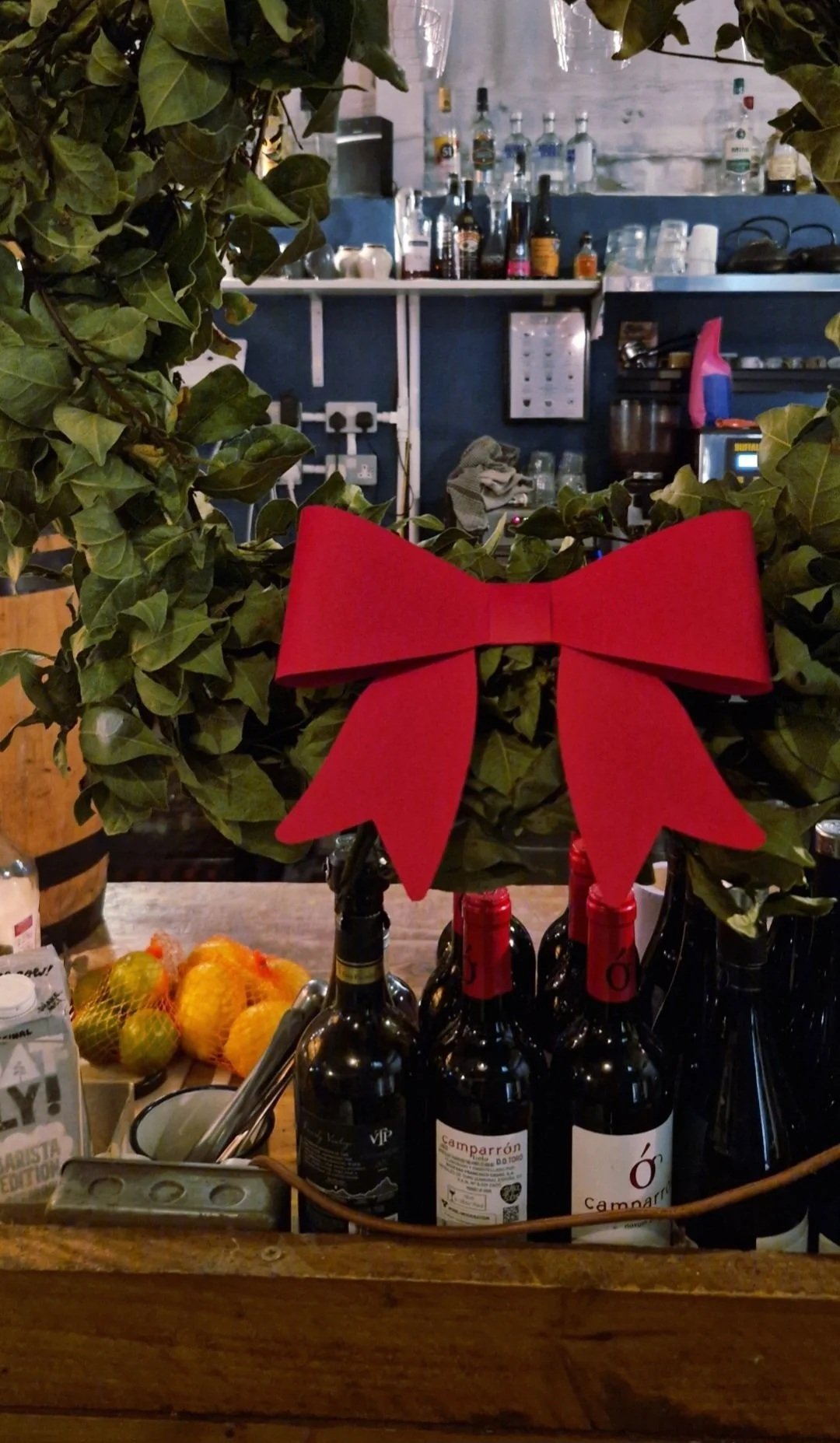 Decorative arrangement of wine bottles with a red Christmas bow on green foliage, in a bar or restaurant setting.