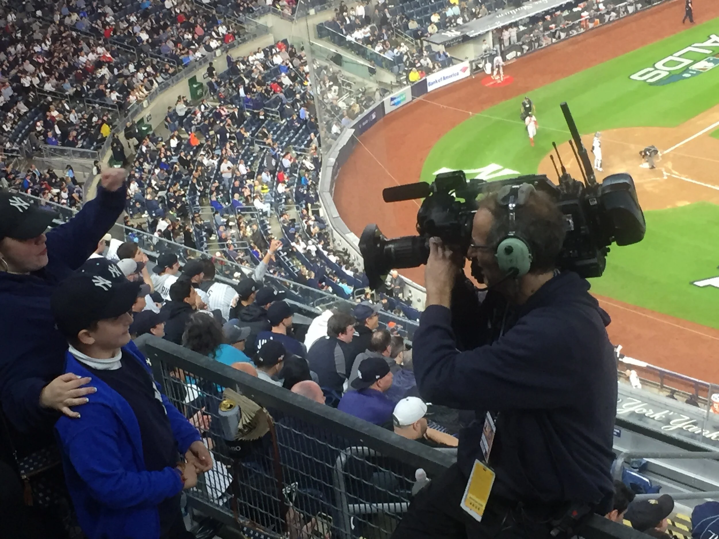 Image of a camera person filming a father and son using a camera-back Wave Central system, set in a crowded baseball stadium