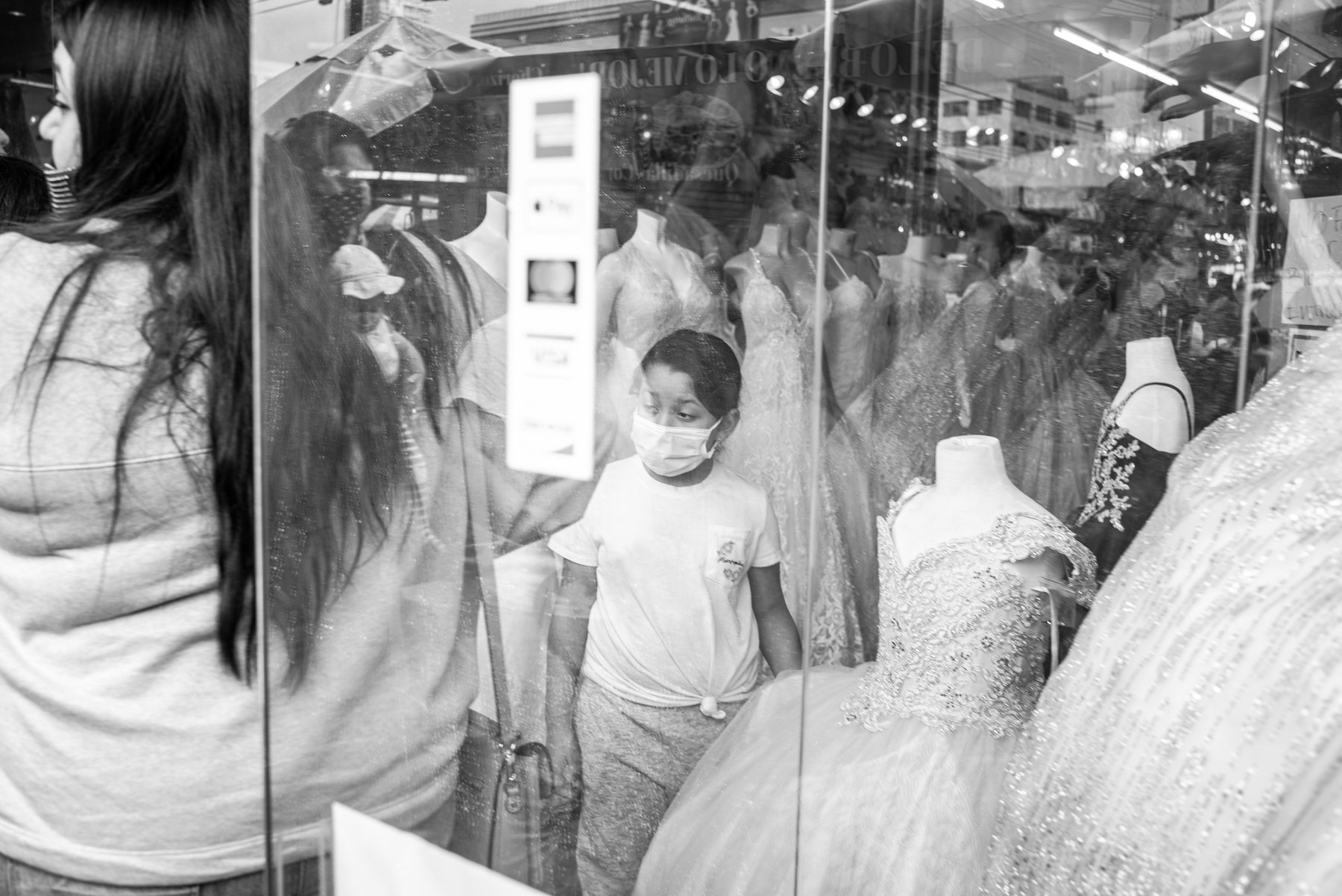  A young girl looks into the crowded street from inside a dress store in the Santee Alley outdoor markets in downtown, as COVID-19 restrictions eased. (Los Angeles, California, 2021). © Pablo Unzueta 