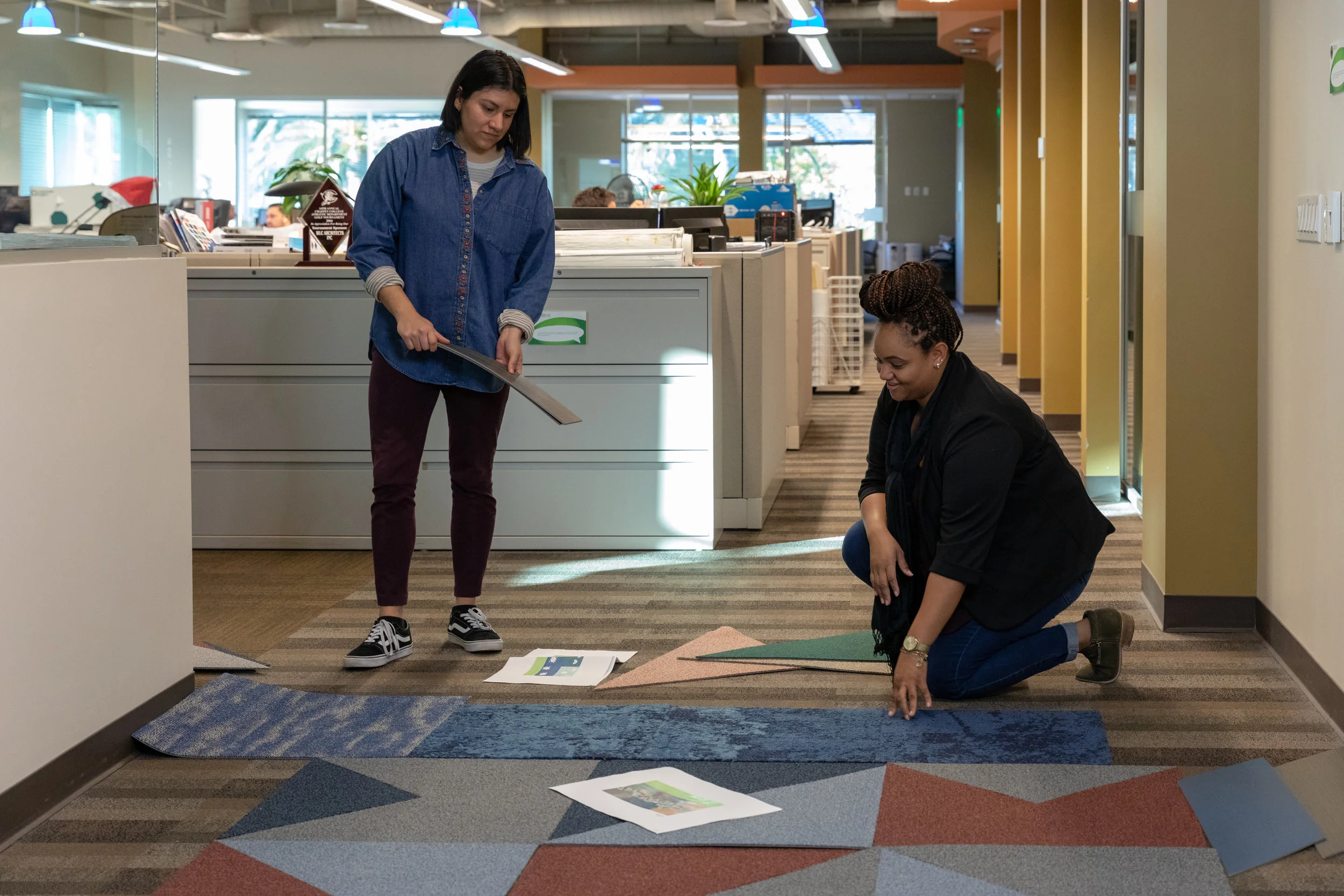Designers Candace Luckett and Daniela Martinez lay out carpet samples during flooring design.