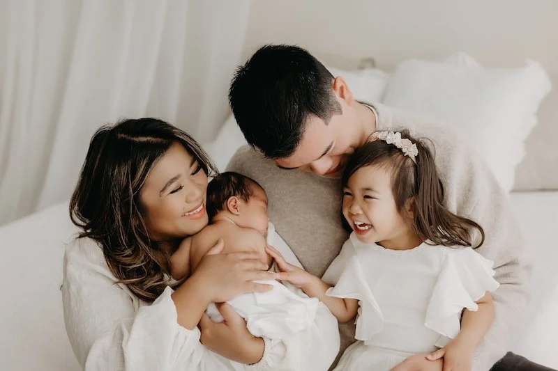 Family of four with a mother, father, a young girl, and a newborn, smiling and enjoying their first family photos with their new baby