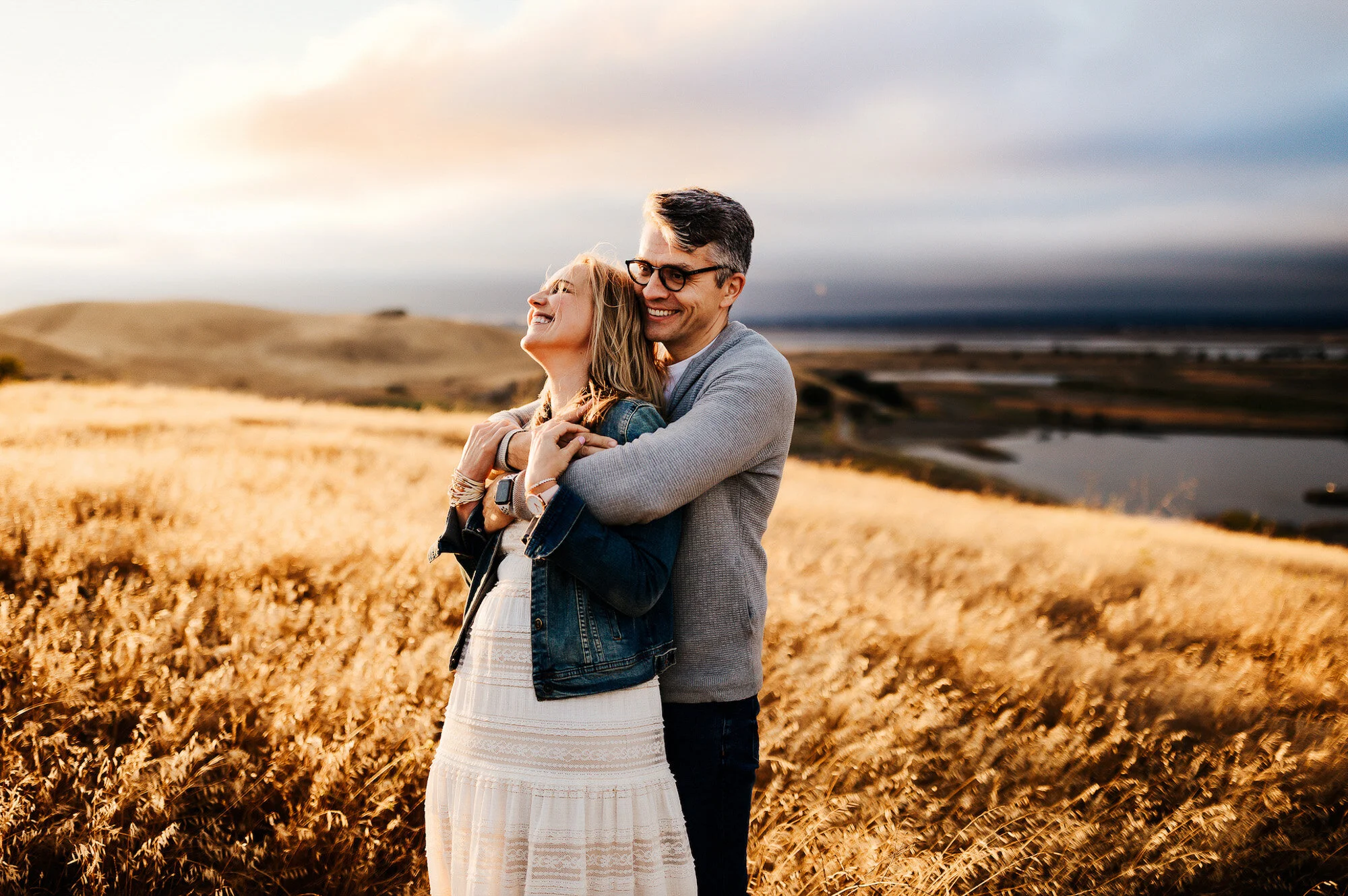 A couple embracing in a golden wheat field at sunset, smiling happily.