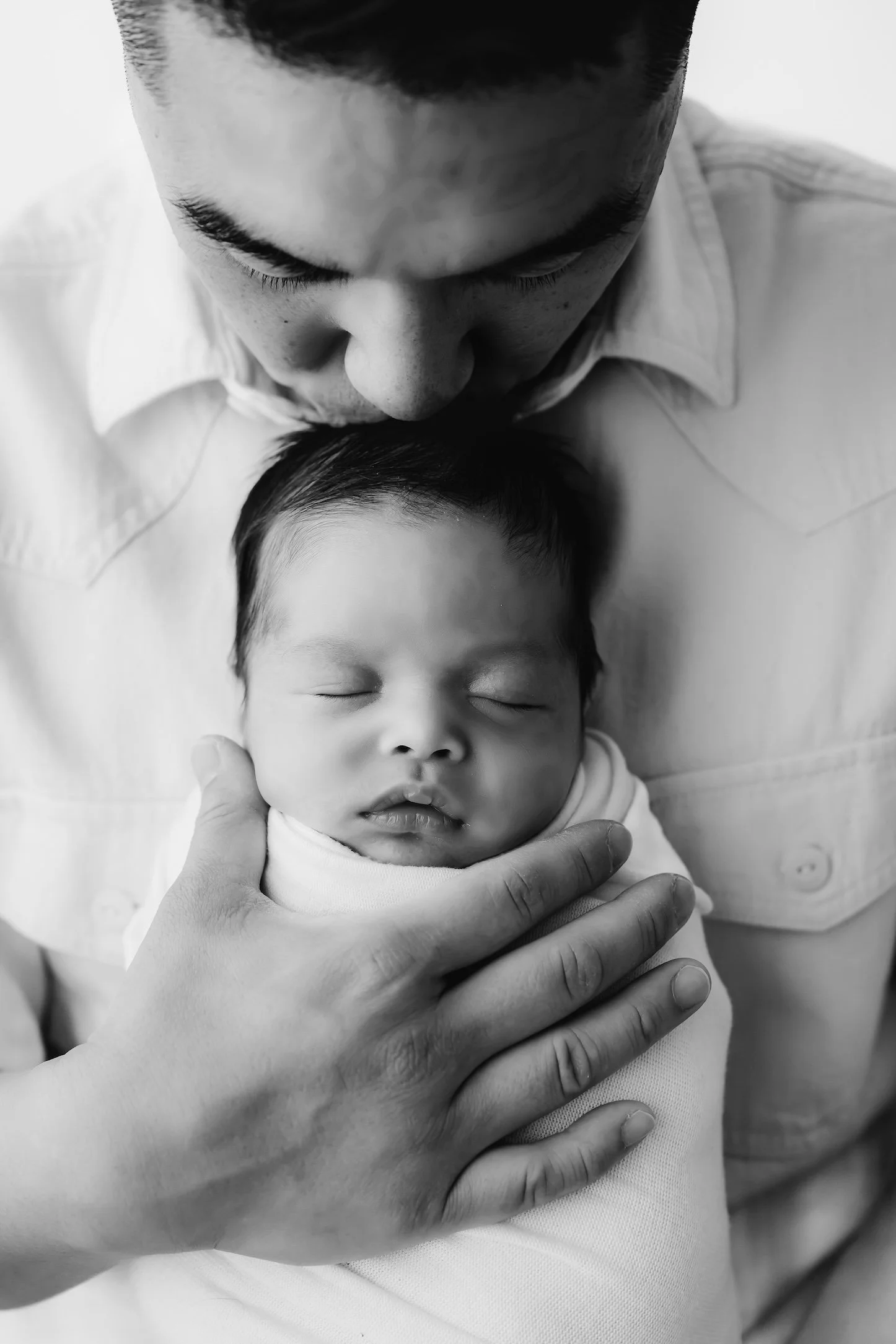 Black and white photograph of an adult holding a sleeping baby close, with the adult looking down at the child.